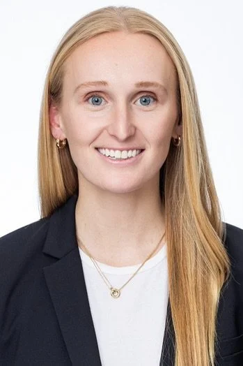 Woman smiling in a professional headshot wearing a black blazer and white top against a plain white background.