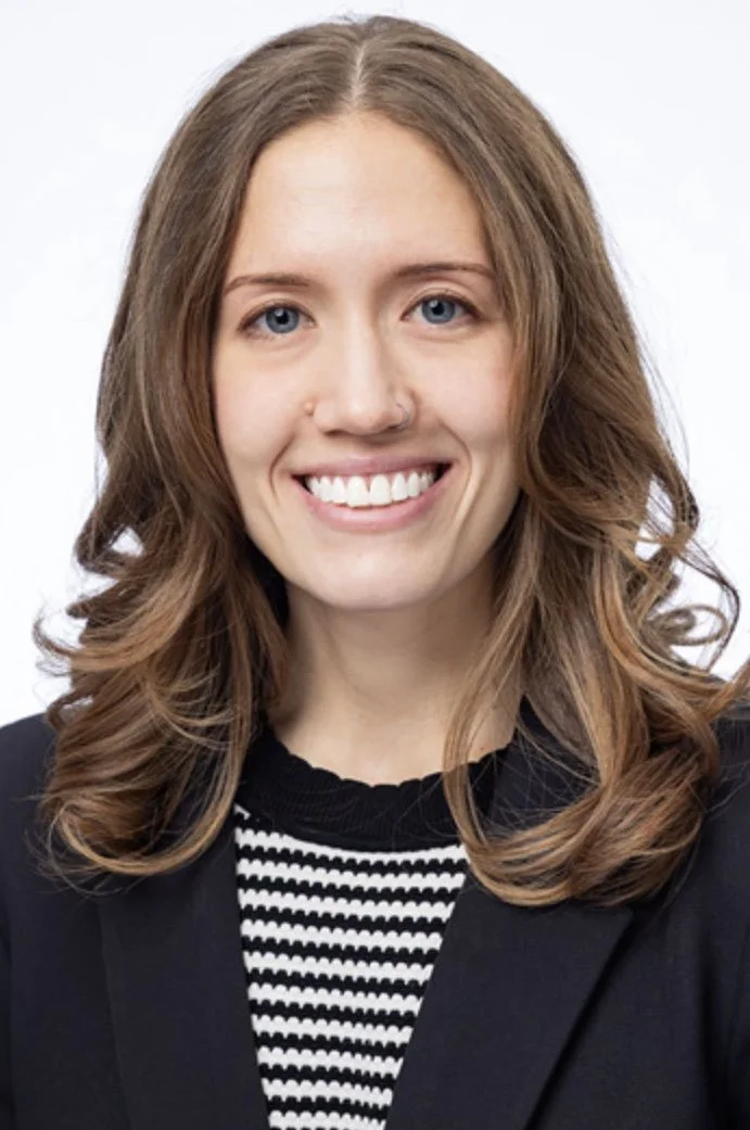 Woman smiling in a professional headshot wearing a dark blazer and striped top against a light background.