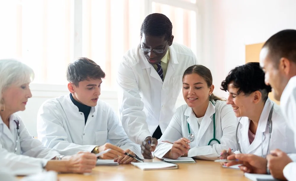 Group of medical students and doctors in white coats collaborating and studying together at a table.