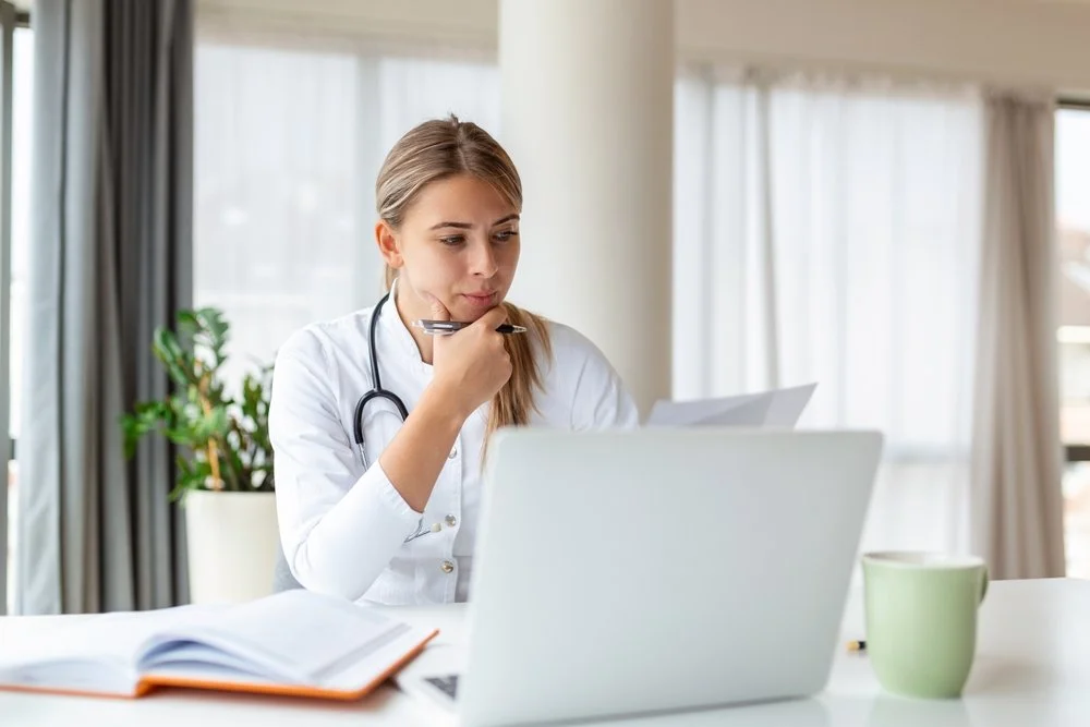 Female medical student reviewing notes while studying on a laptop at a desk.