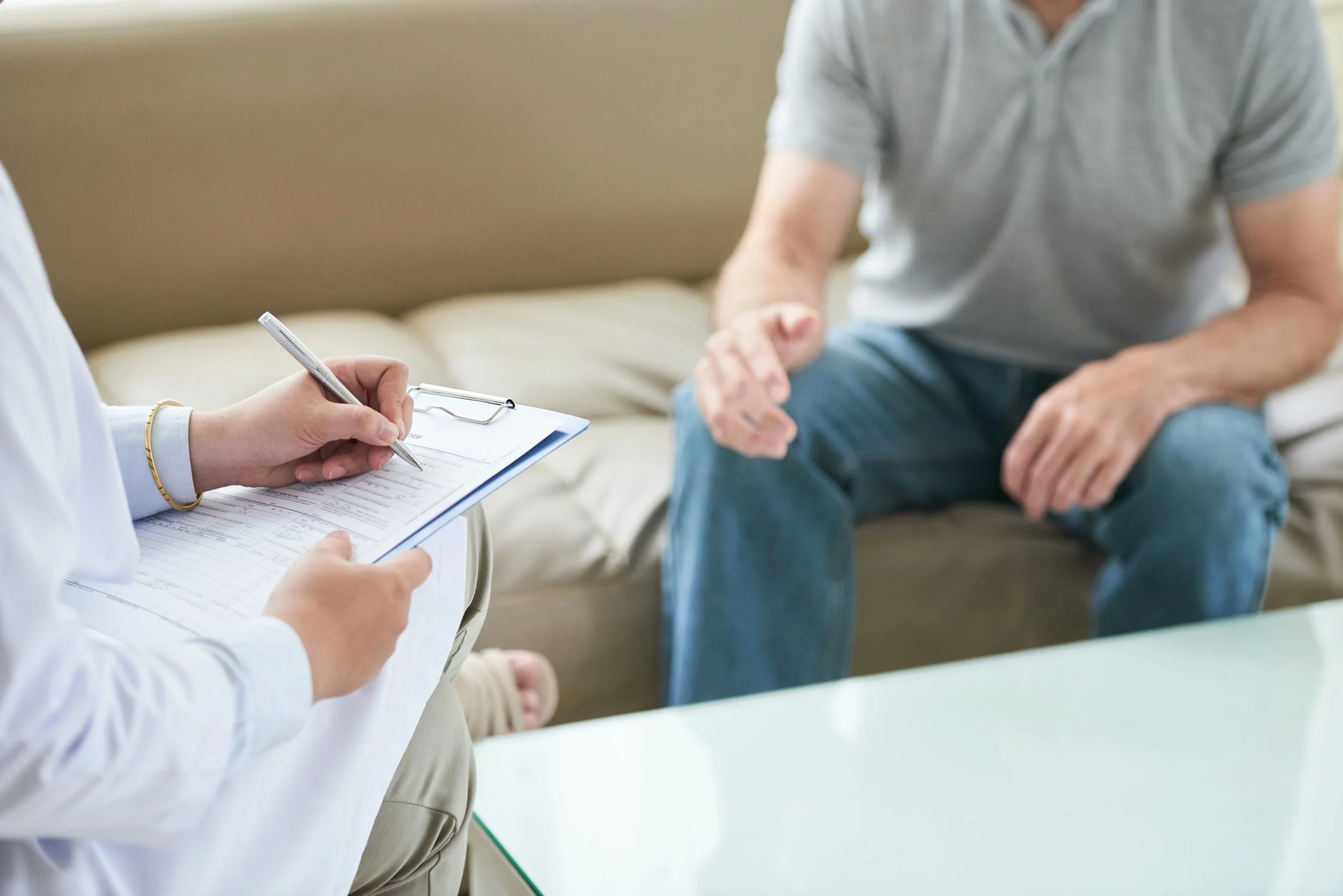 Doctor taking notes on a clipboard while speaking with a patient during a medical consultation.