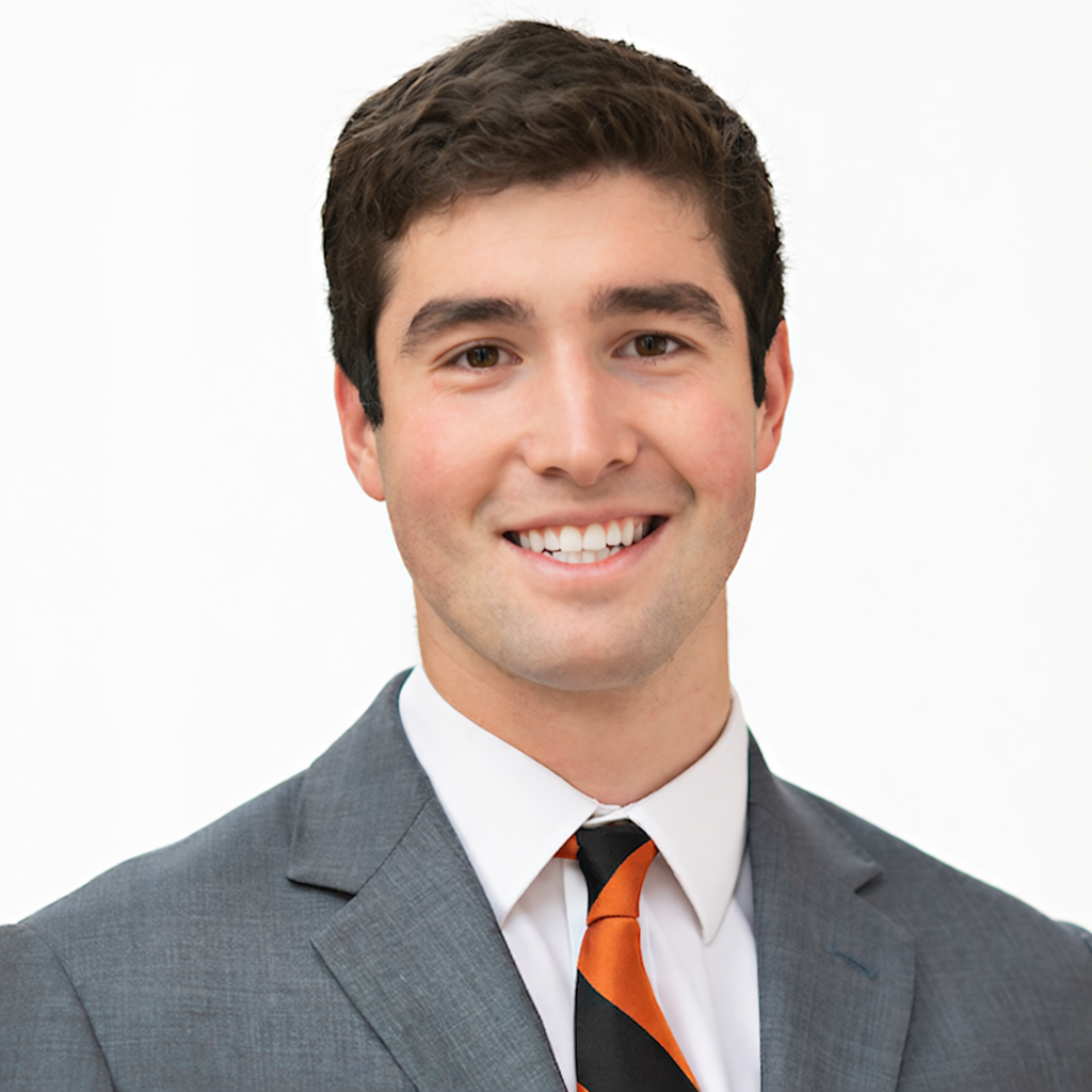 Man smiling in a professional headshot wearing a gray suit, white shirt, and orange-and-black striped tie against a plain white background.
