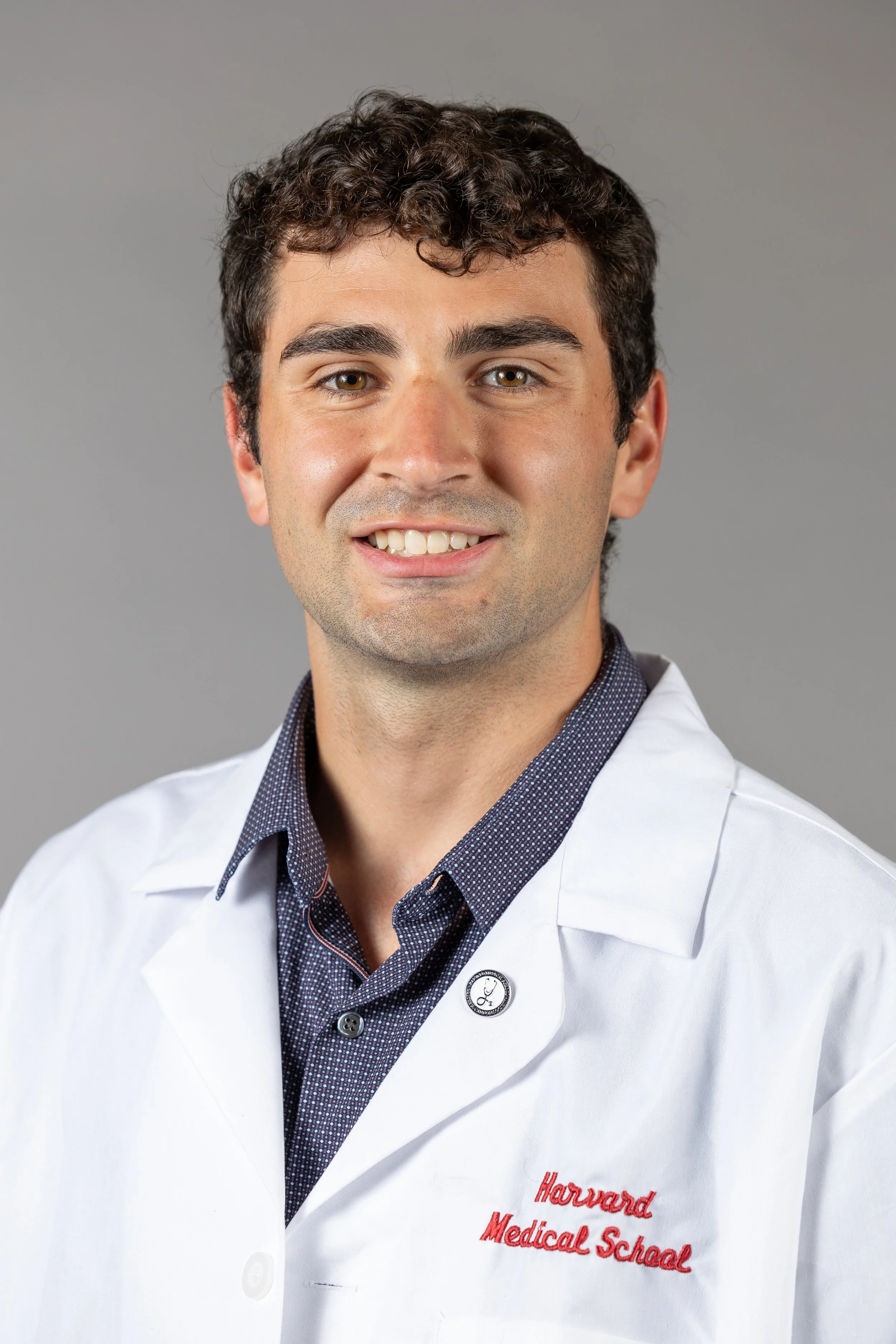 Man smiling in a professional headshot wearing a white medical coat against a gray background.