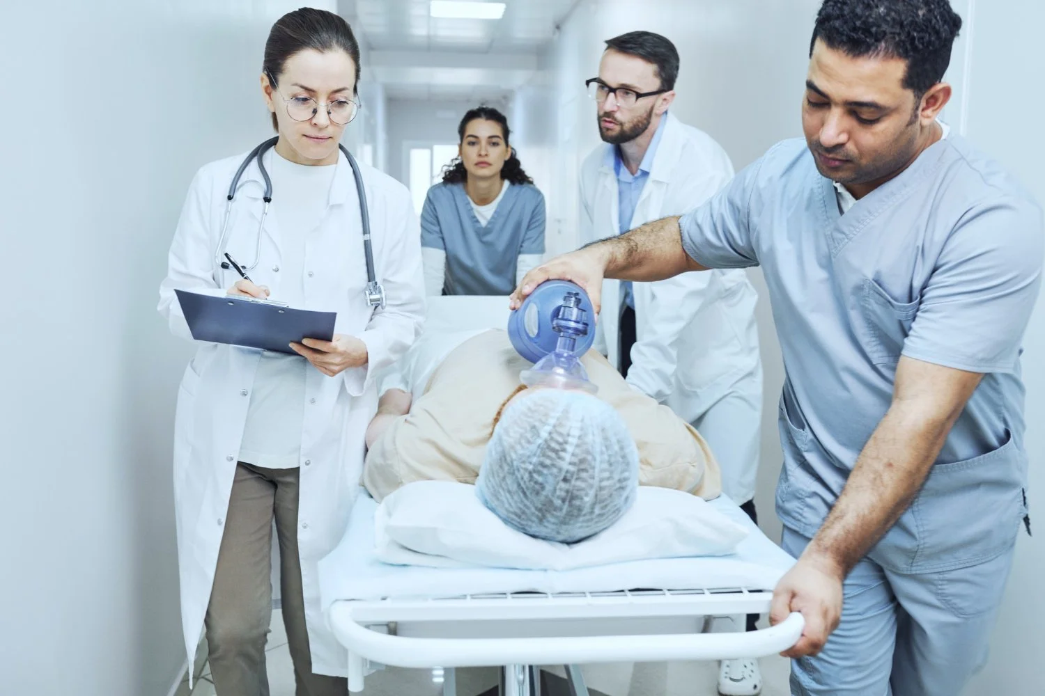 Medical team providing emergency care to a patient on a hospital gurney while manually ventilating with a bag-valve mask.