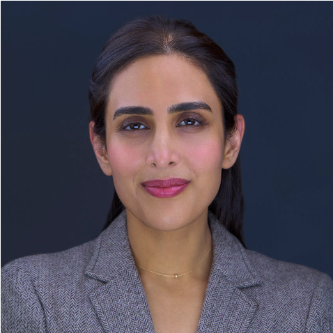 Woman smiling in a professional headshot wearing a gray blazer against a dark blue background.