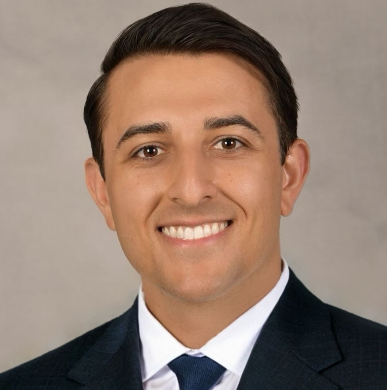 Man smiling in a professional headshot wearing a dark suit and tie against a neutral background.