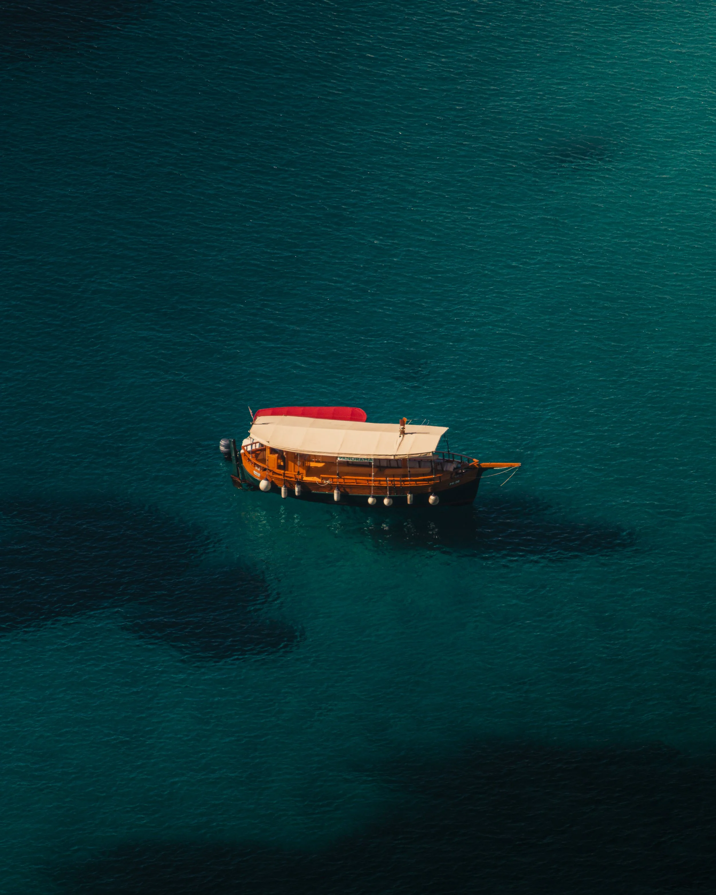 A small wooden boat with a beige canopy floating on calm blue waters.