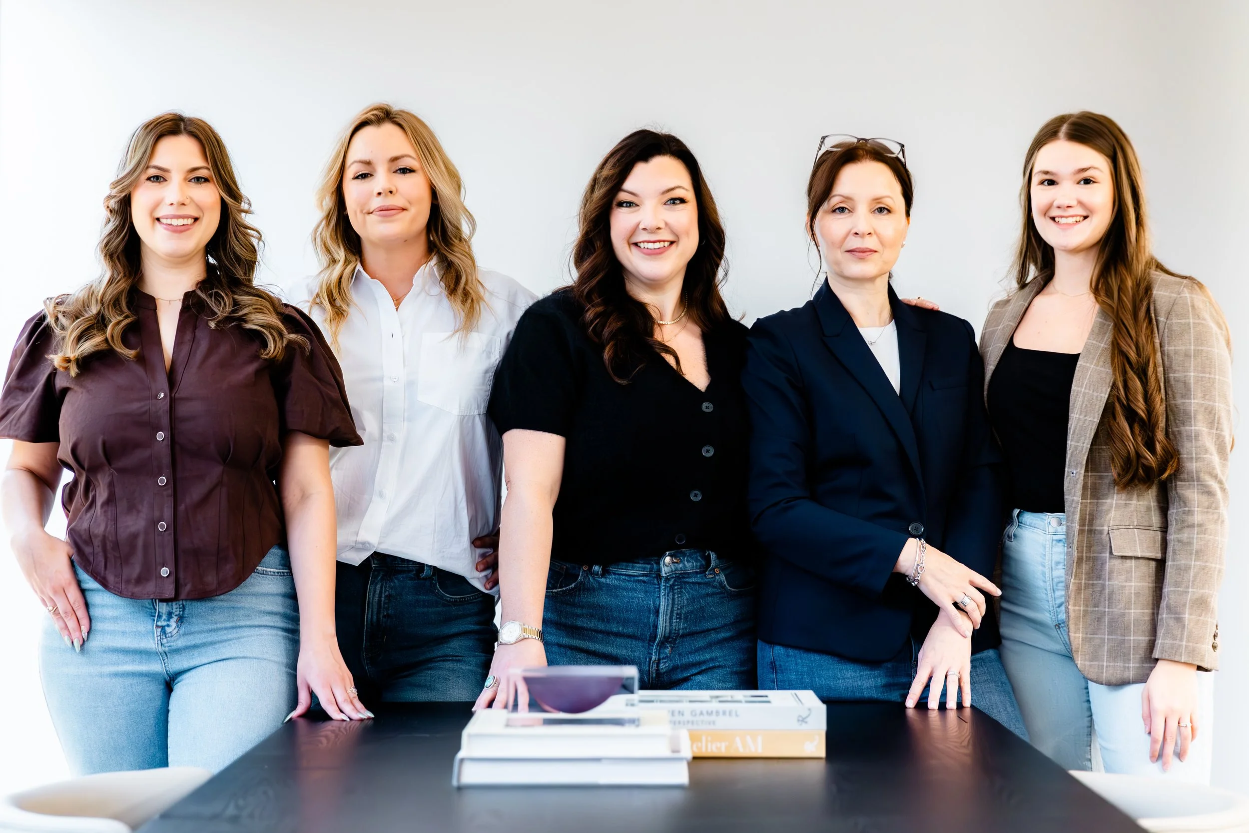 Group of five professional designer and architect women standing together in an office setting, smiling at the camera.