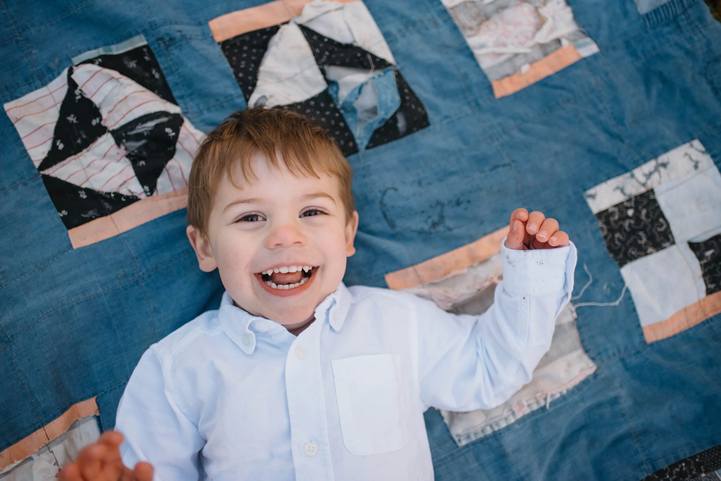 Young boy sitting on concrete steps, smiling, wearing a blue plaid shirt, jeans, and sneakers.