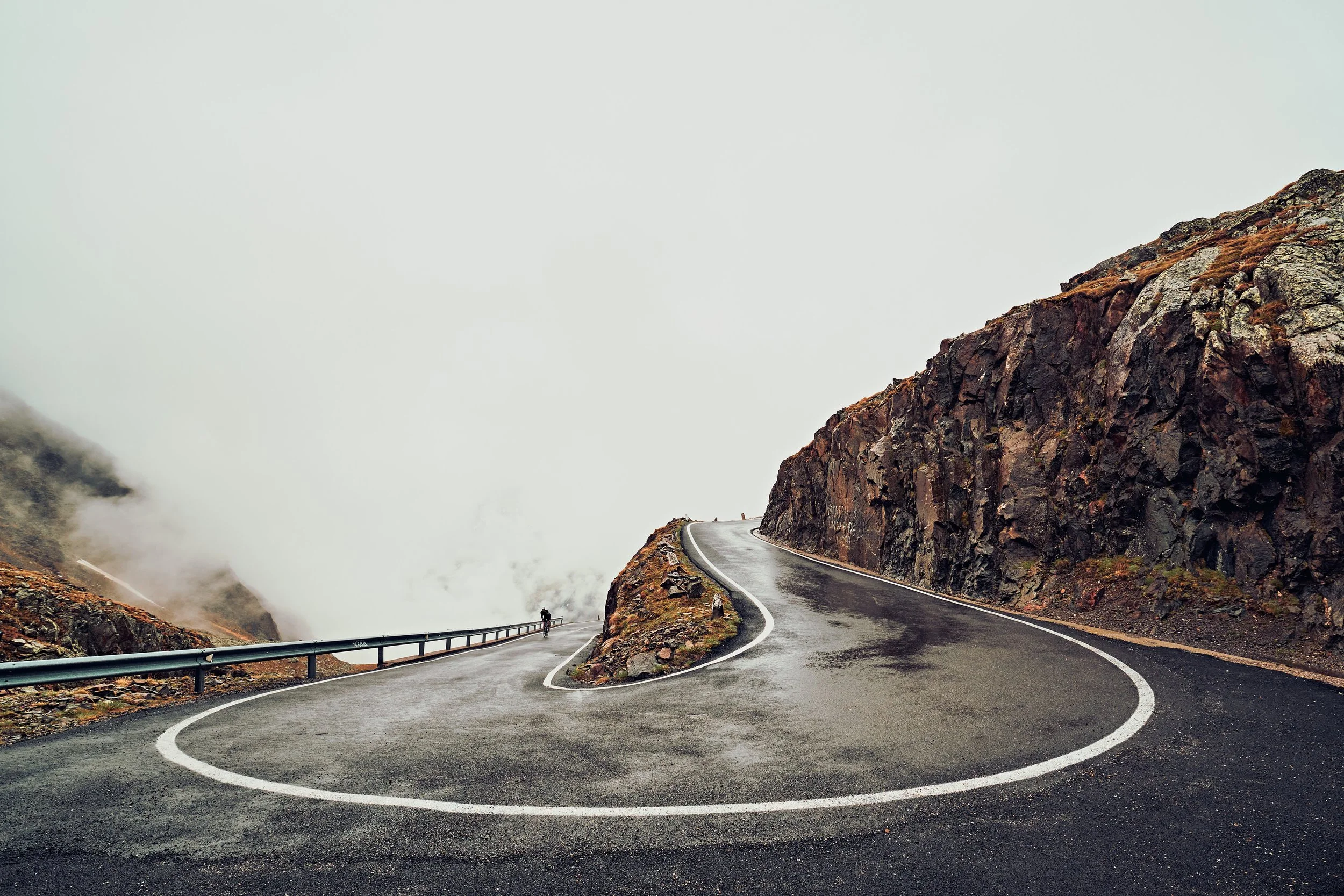 Cyclist riding up an alpine road amidst rocky landscape on the way to the summit.