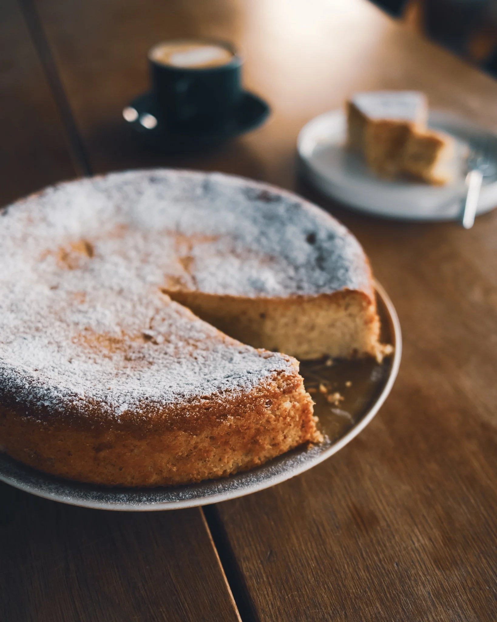 Ricotta, almond and polenta cake, placed on a wooden table next to a cup of coffee.
