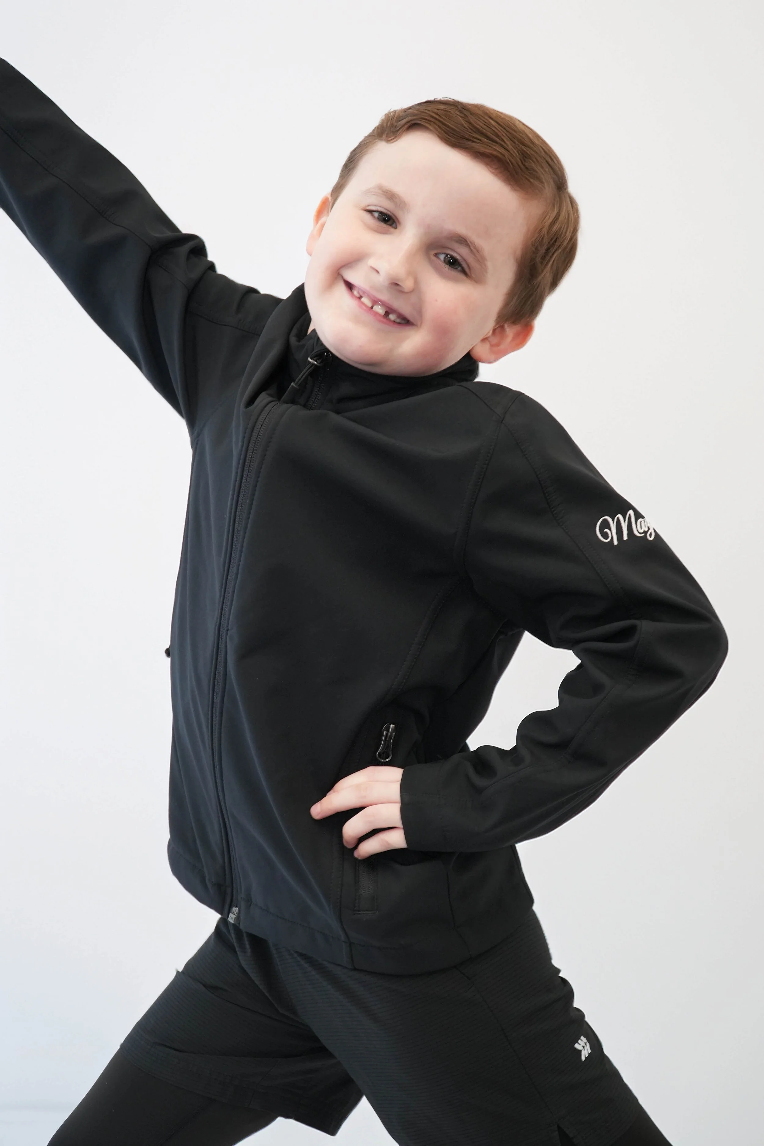 Young boy kneeling against a black background, with green and white lighting on his face and shirt, looking upward.