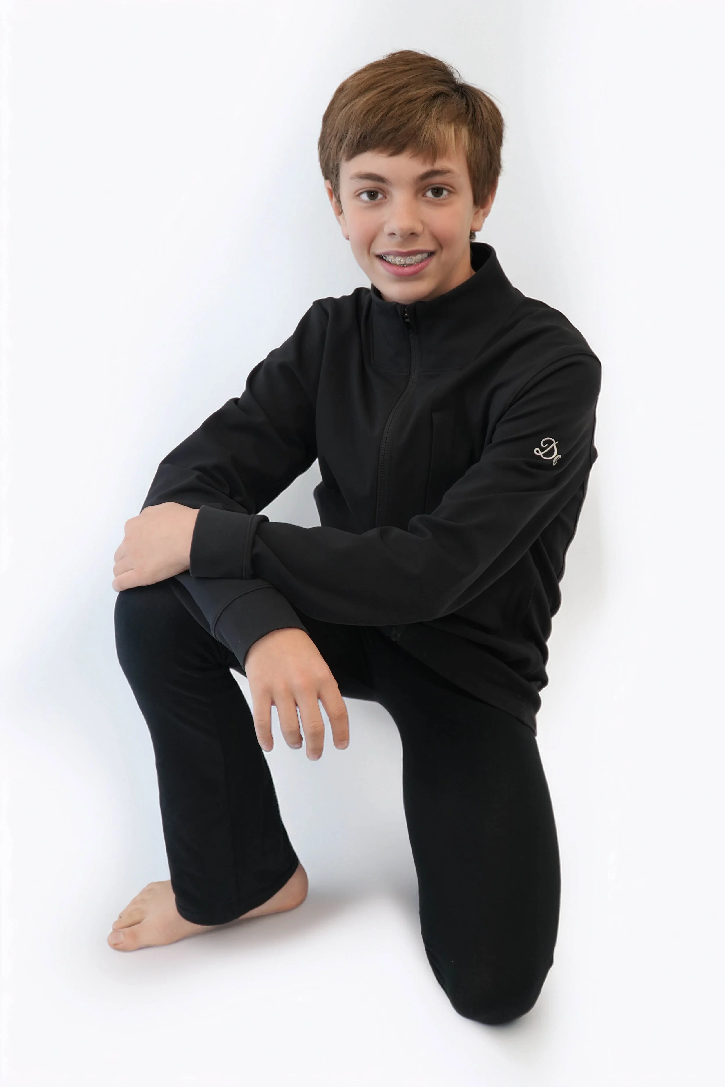A young boy in a white long-sleeve shirt and pants is crouching against a dark background with green lighting.