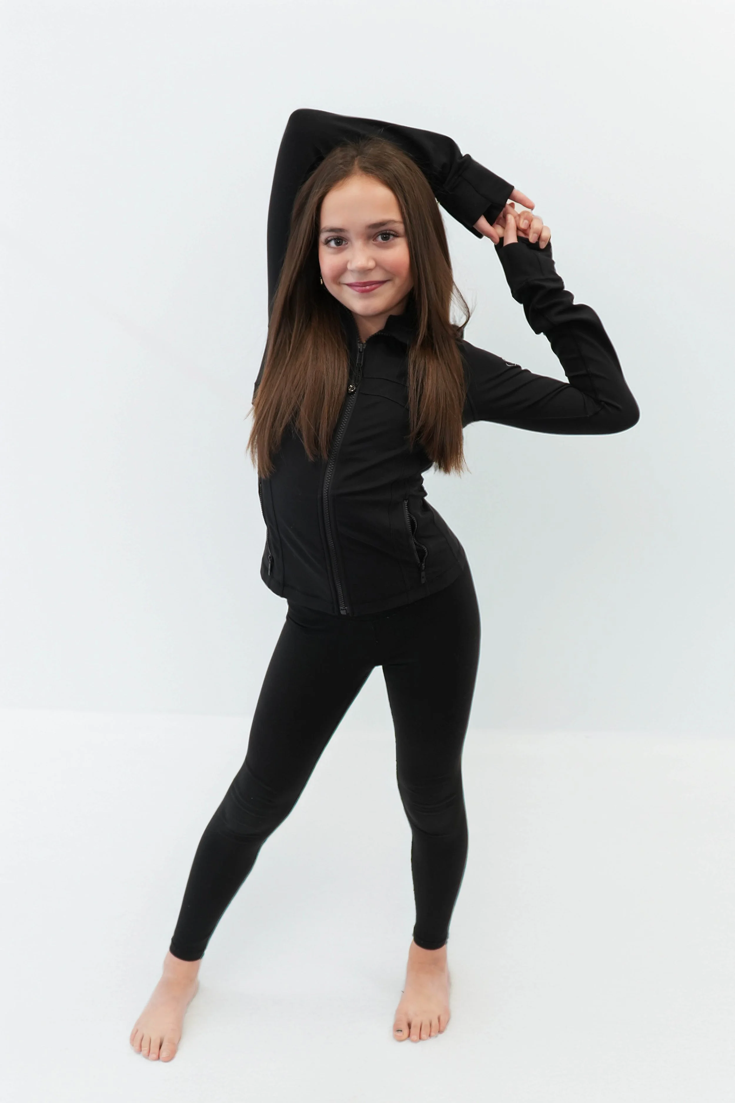 A young girl with long brown hair in a white outfit striking a pose against a dark background, illuminated with green lighting.