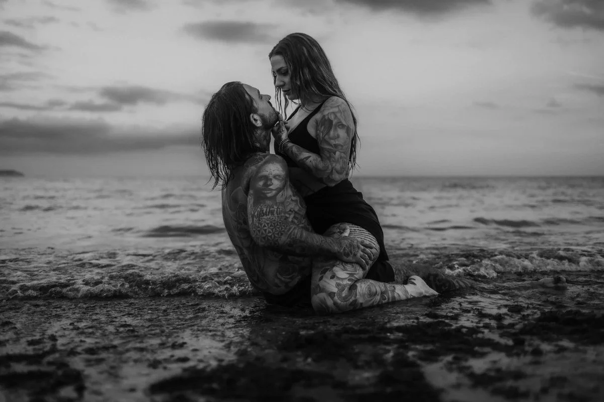 Black and white couples portrait of two people embracing in the shallow sea on a beach under a moody overcast sky