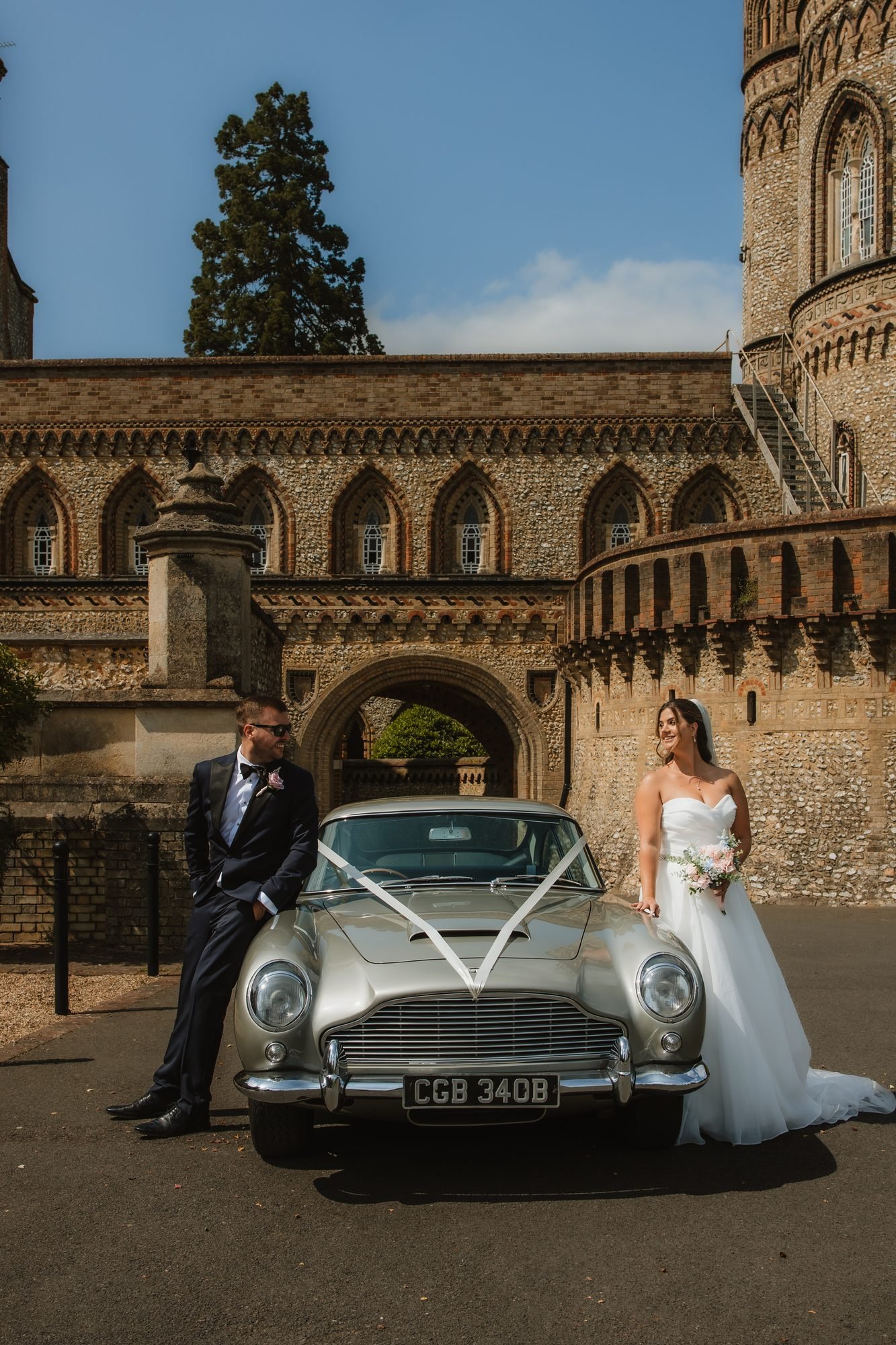 Bride and groom beside a vintage silver Aston Martin at a castle wedding venue