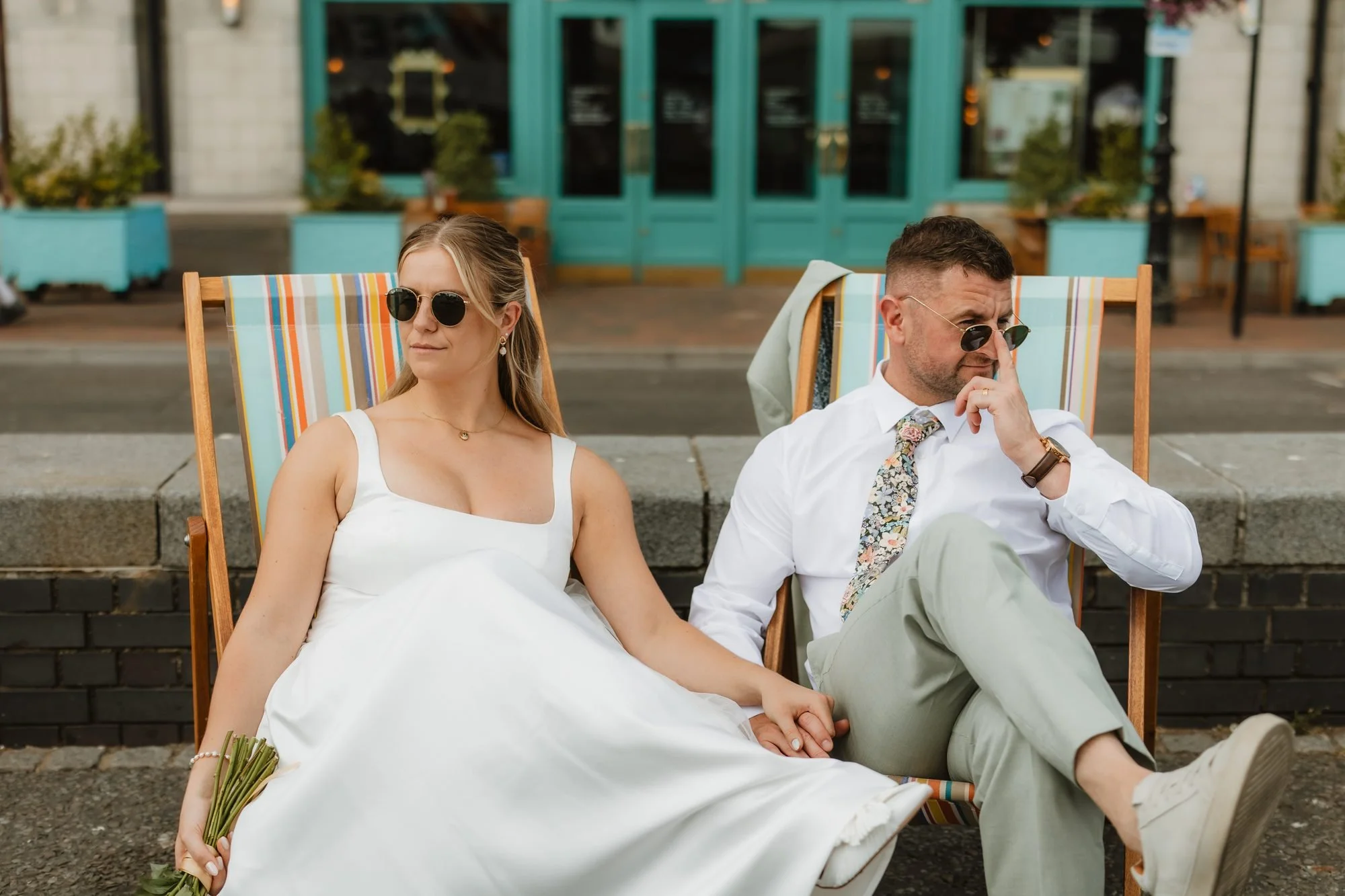 Bride and groom relaxing in deckchairs wearing sunglasses on their wedding day