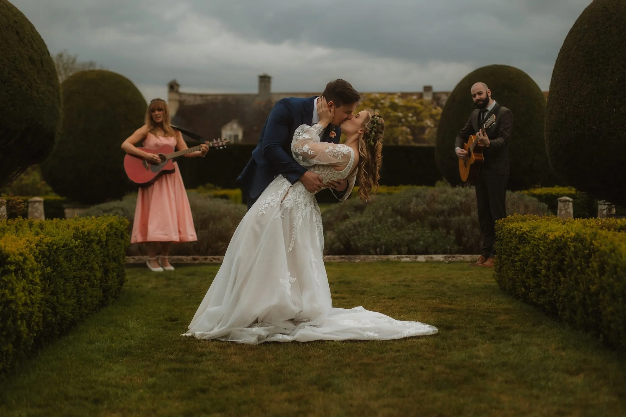 Groom dipping the bride for a kiss in a formal garden while musicians play