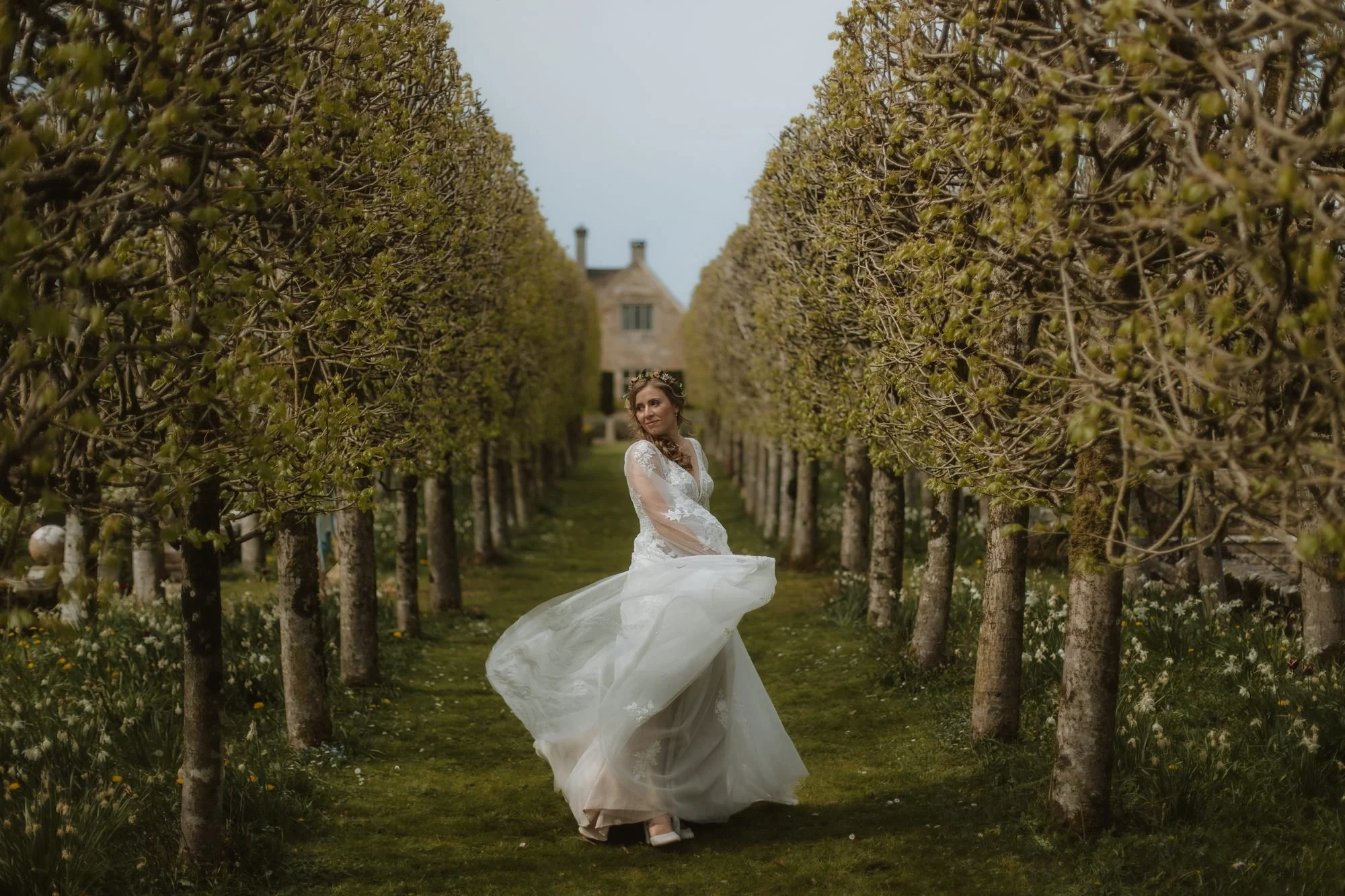 Bride twirling in her dress along an avenue of trees