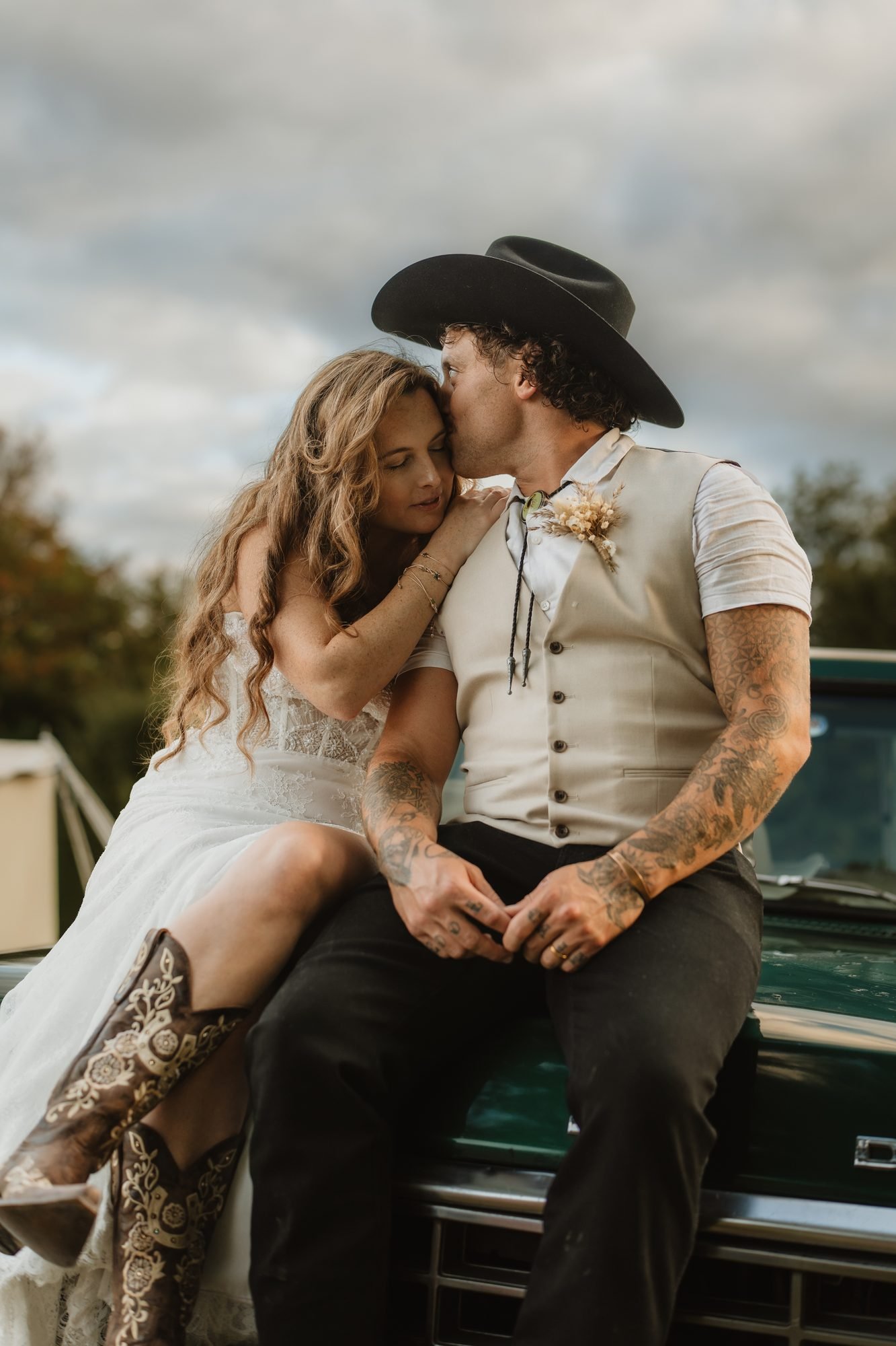 Tattooed groom in a cowboy hat with his bride sitting on a vintage pickup truck