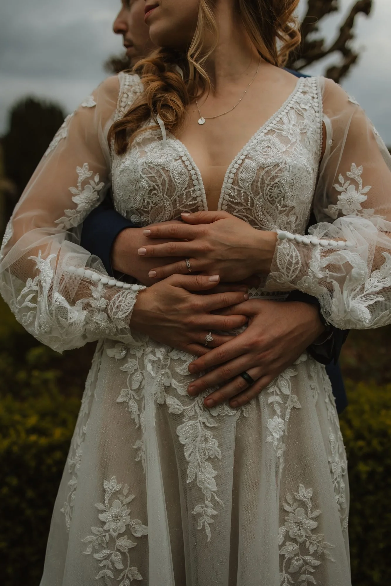 Close-up of the groom's hands around the bride's lace wedding dress