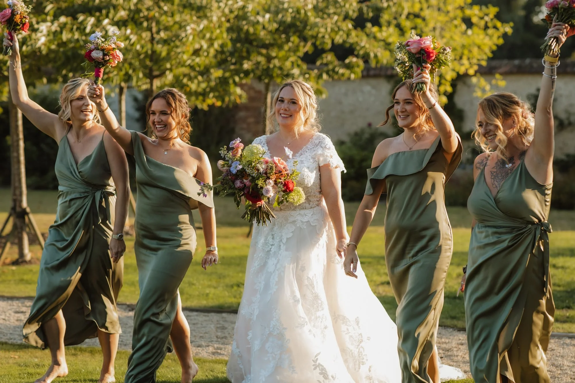 Bride and bridesmaids in sage green dresses cheering with bouquets raised