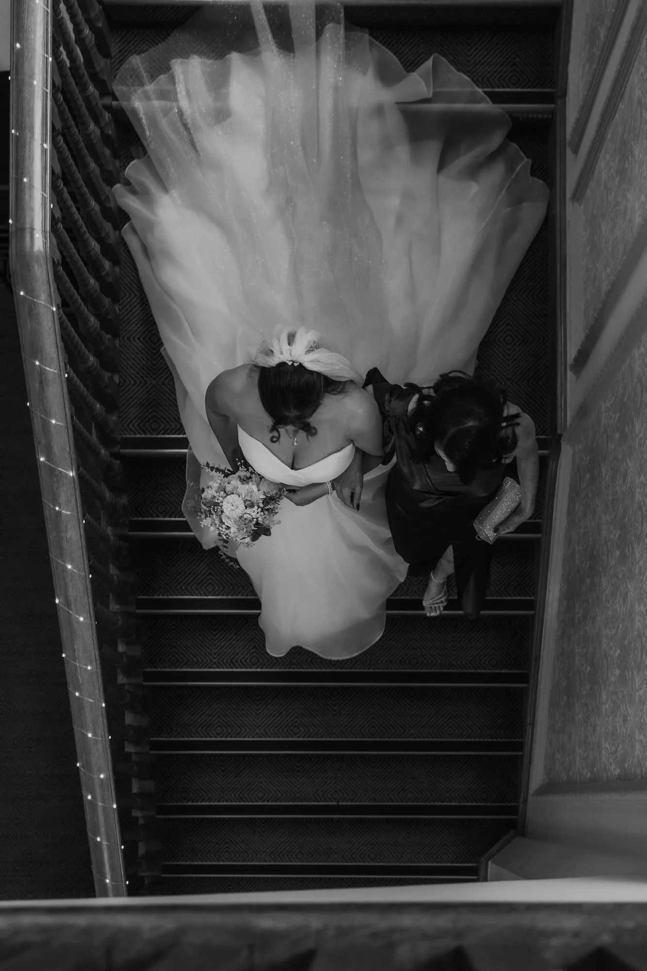 Black and white view from the top of a spiral staircase looking down on the bride and groom