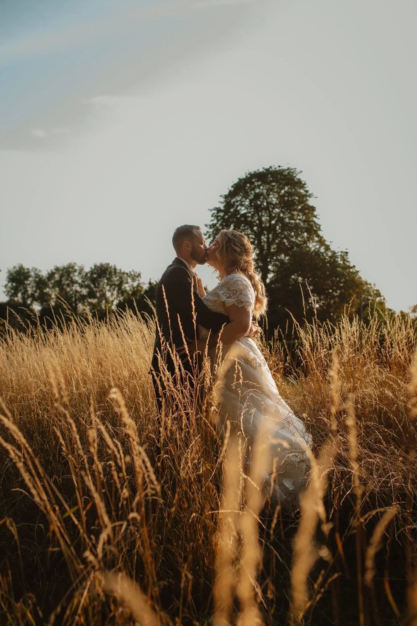 Bride and groom kissing in long golden grass at golden hour