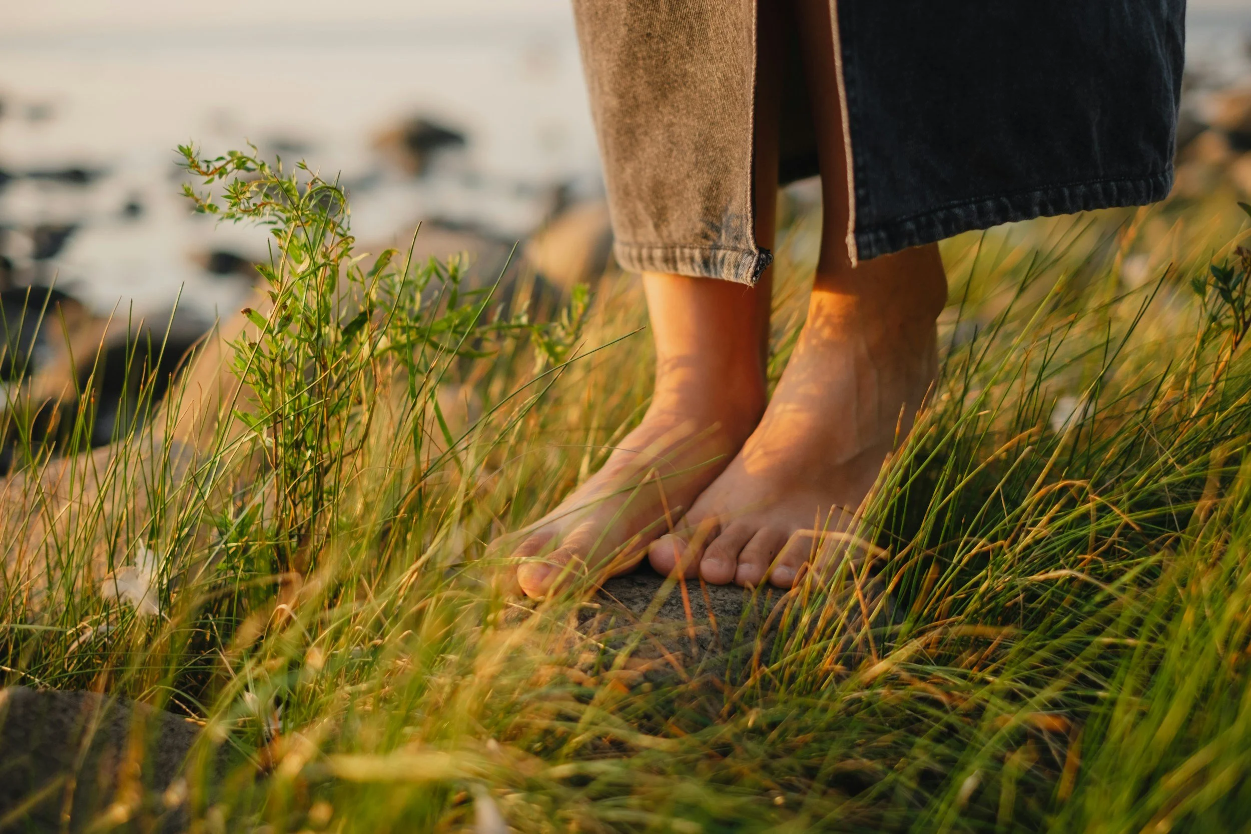 Barefoot person standing on grassy ground near rocks, with a blurred background.