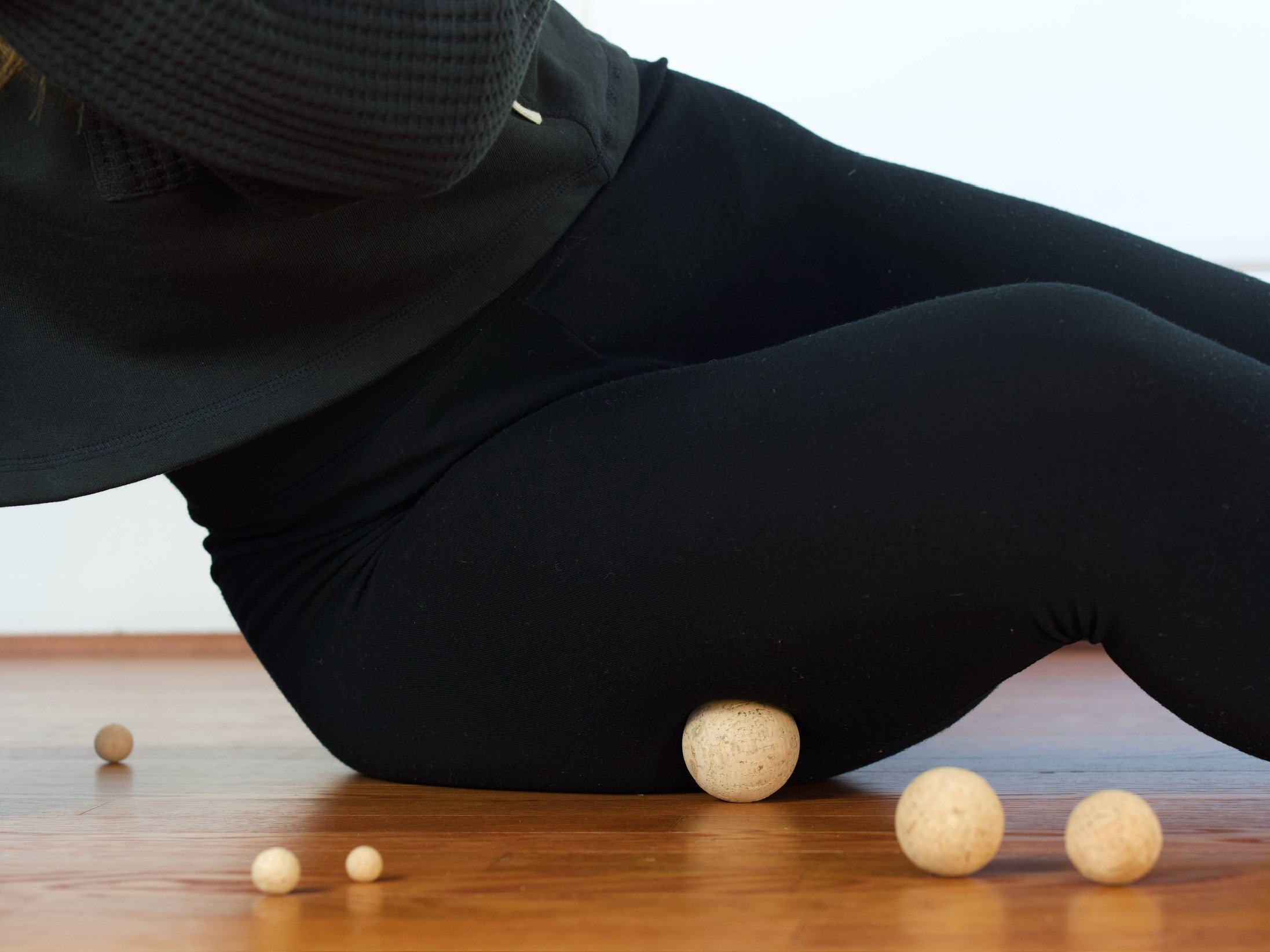 A person in black clothing kneeling on a wooden floor, surrounded by several small wooden balls.