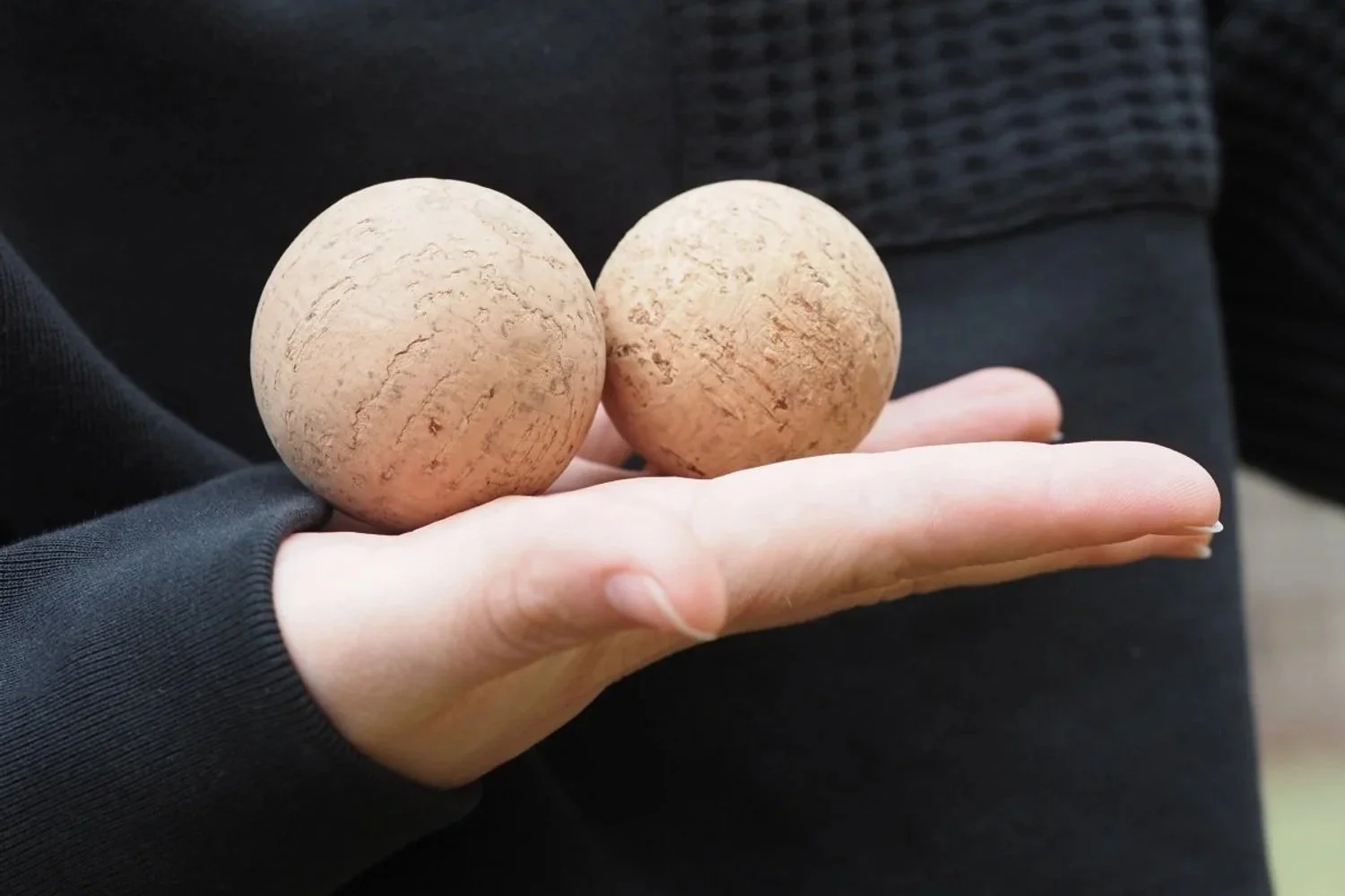 A hand holding two spherical, textured, light brown objects that resemble stones or planet models.