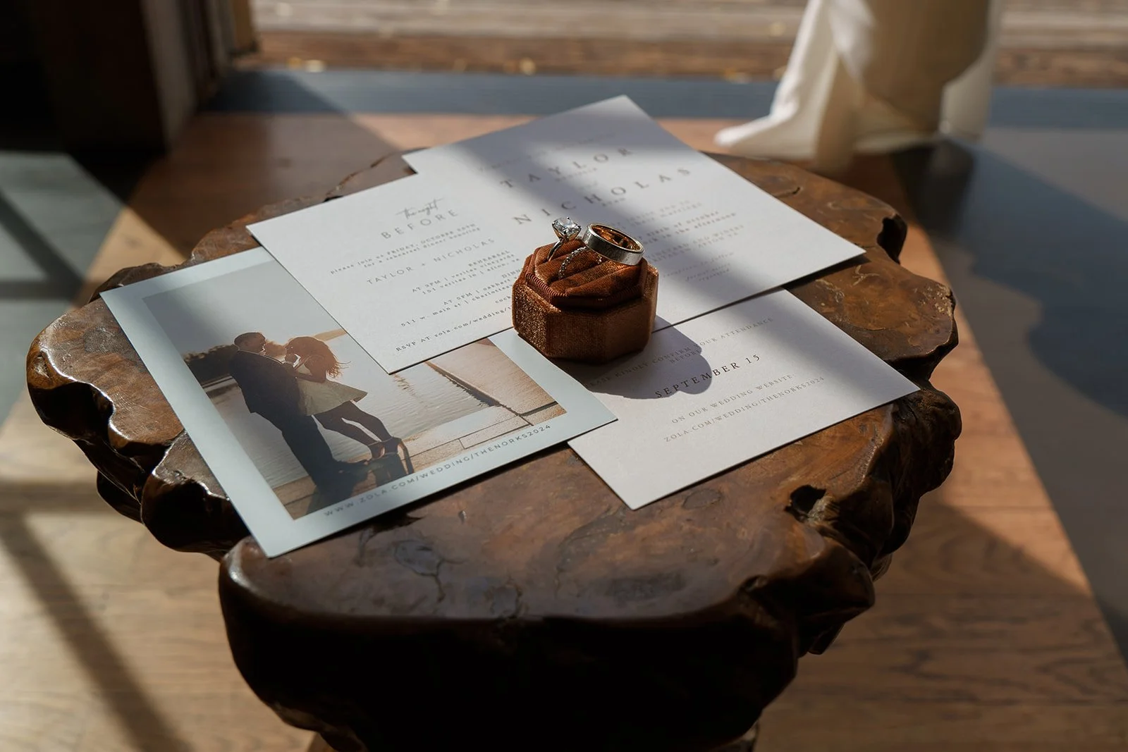 Wedding invitation, a photograph of a couple, and wedding rings on a rustic wooden table.