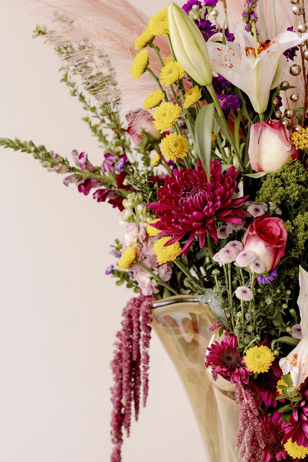 Close-up of a colorful flower arrangement in a vase, featuring white lilies, pink roses, yellow chrysanthemums, purple flowers, and lush green foliage.