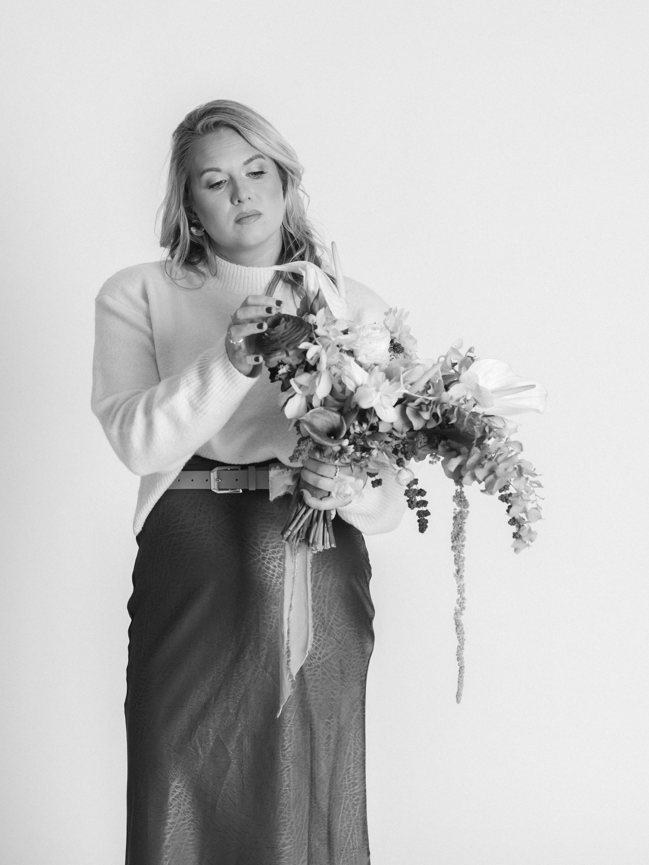 A woman in a sweater and skirt holding a large bouquet of flowers and arranging them.