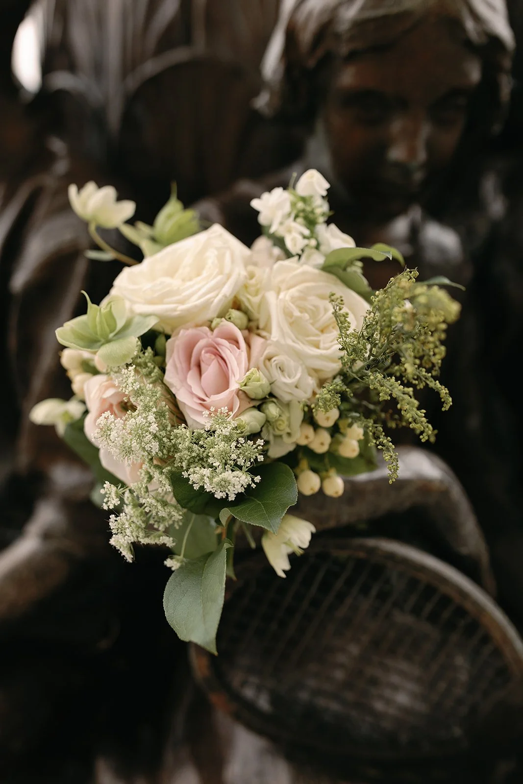 A person holding a bouquet of white, pink, and green flowers in front of a dark, wooden background.