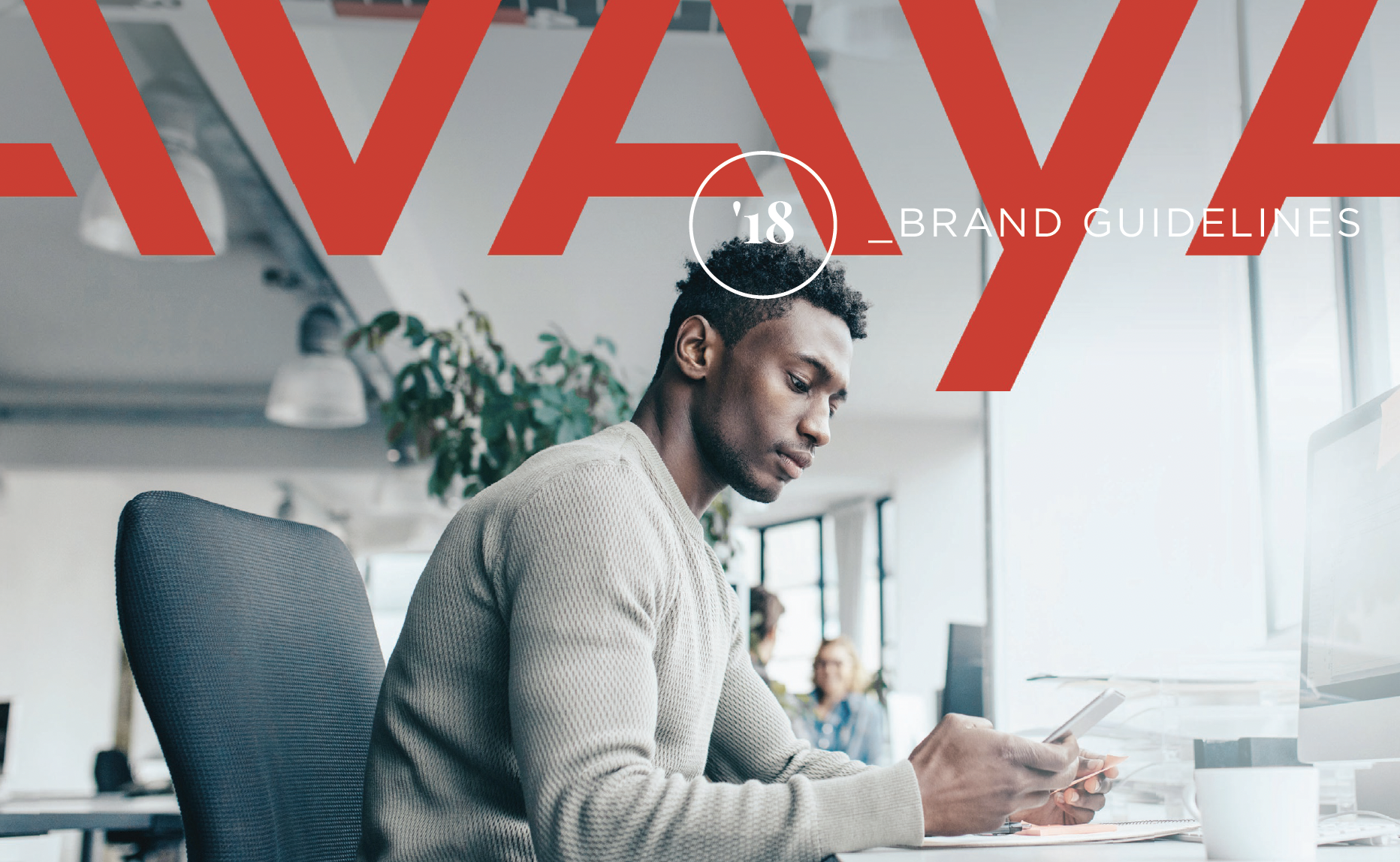 A young man with curly hair wearing a beige sweater, sitting at a desk in an office, looking at his smartphone. Other people are working in the background, and there is large red text over the image that says 'HAVE' with an overlay of the number 18 and the words 'BRAND GUIDELINES'.