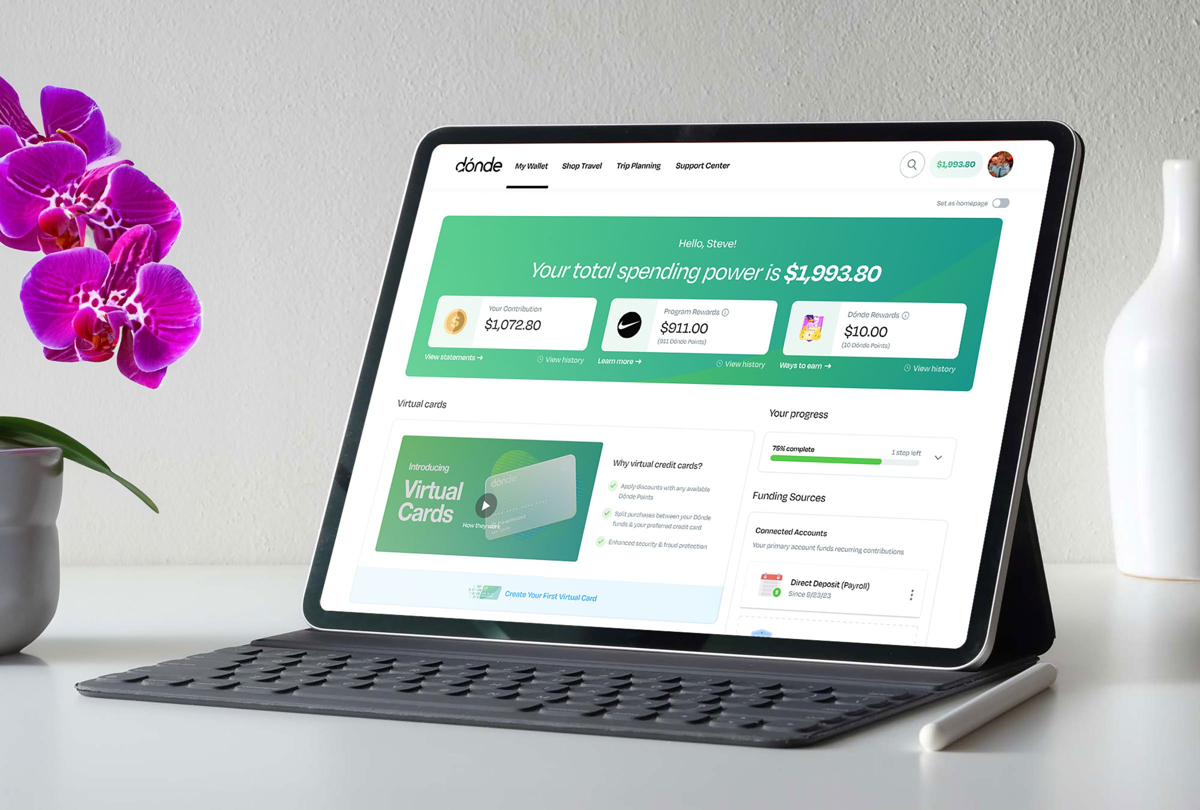 A tablet displaying a financial dashboard with a green background, text showing total spending power of $1,993.80, and various contribution and reward details. The tablet is on a white desk next to a white vase with pink and purple orchids and a white pen.