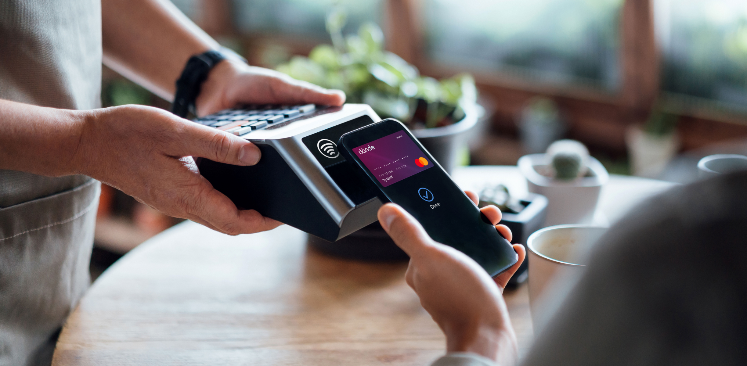 Person using a smartphone to make a contactless payment with a credit card on a payment terminal.
