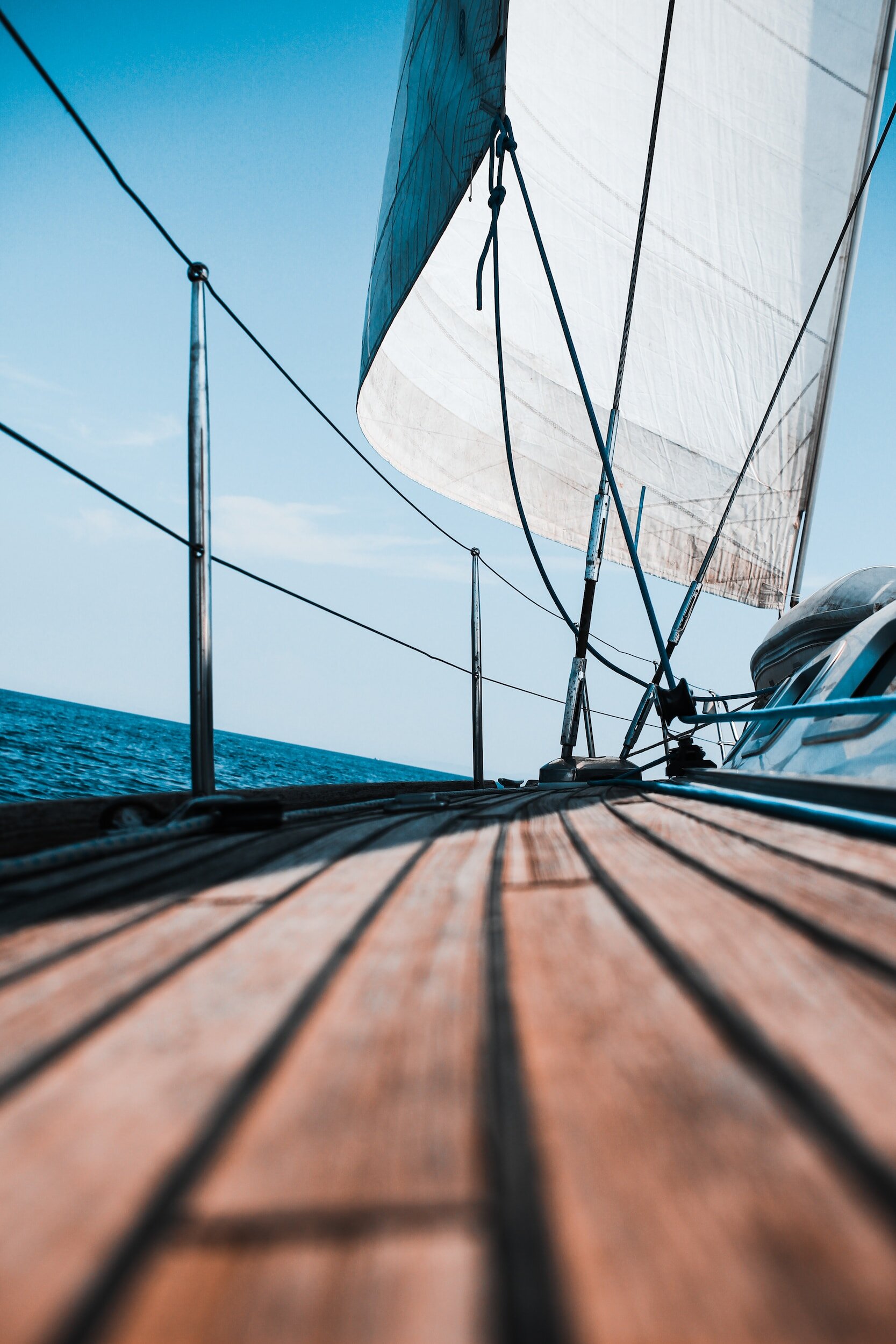 Close-up view of a sailboat deck with sails and rigging, sailing on the ocean under a blue sky.