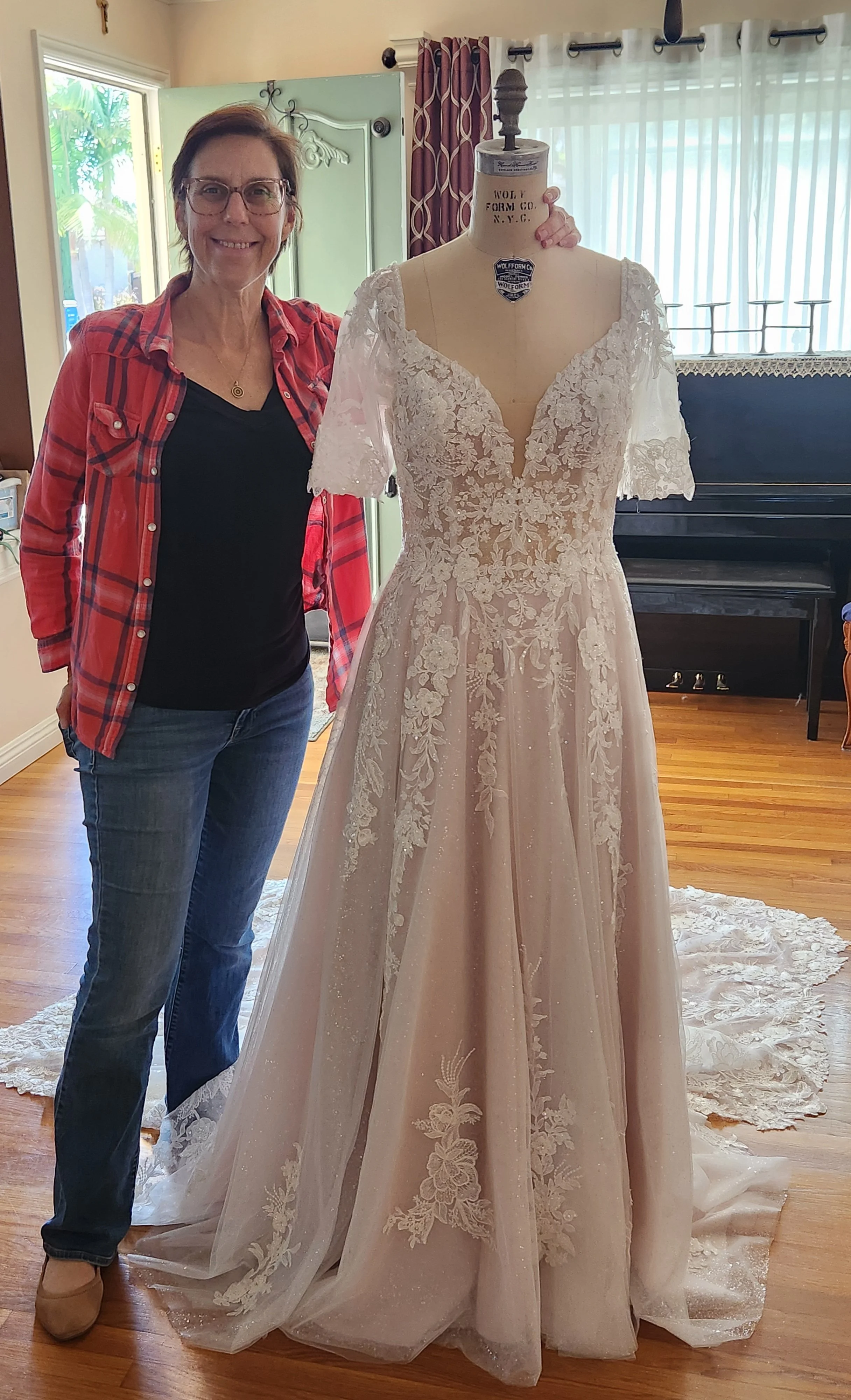 Bridal fashion designer Olga standing with a bridal lace gown, redesigned dress by adding removable sleeves.
