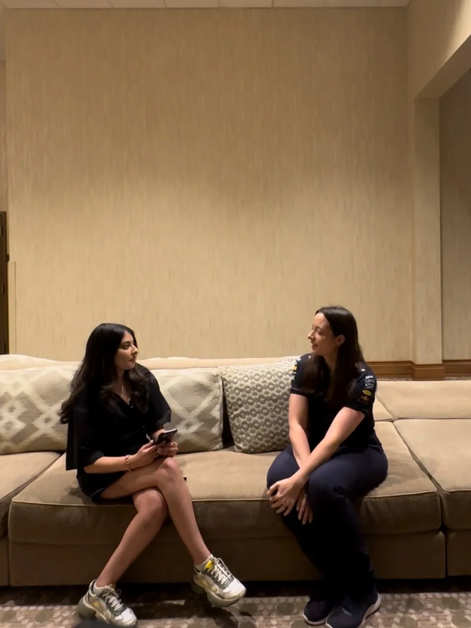 Two women sitting on a beige sofa and having a conversation in a hotel lobby or lounge area.