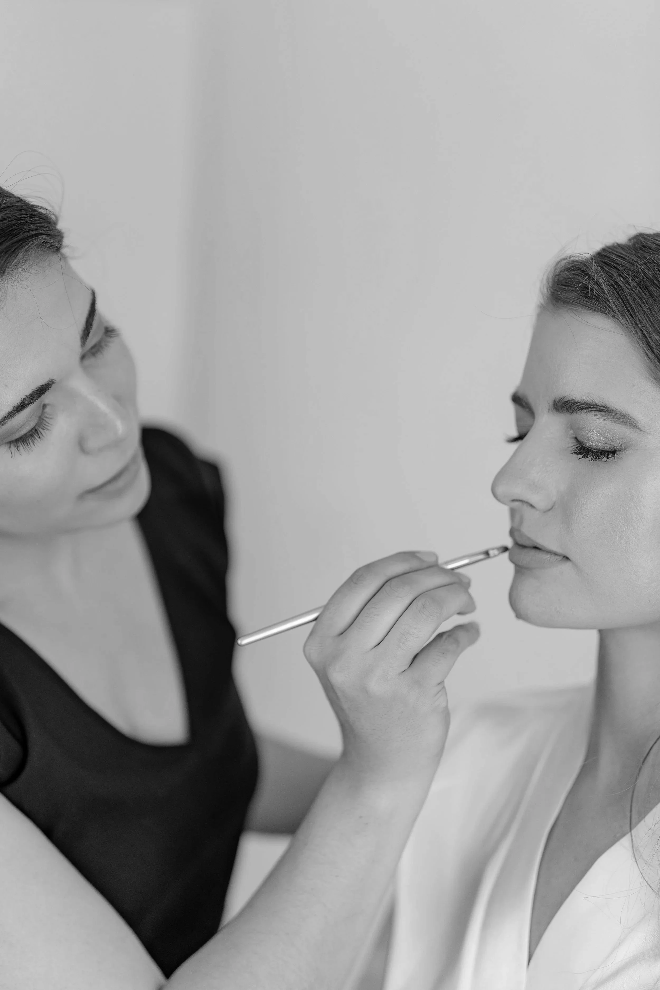 A makeup artist applying lipstick to a woman's lips.