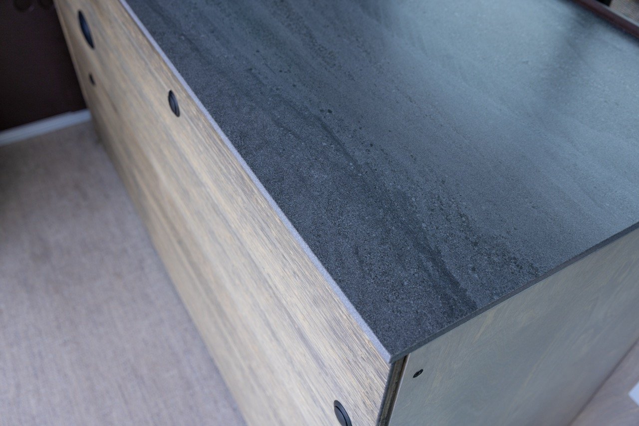 Close-up of a wooden cabinet with a black countertop, showing part of the top and front panel.