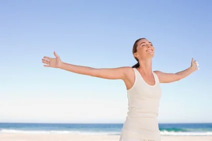 A happy woman standing on the sand at the beach, hands outstretched, smiling face and it is a beautiful day