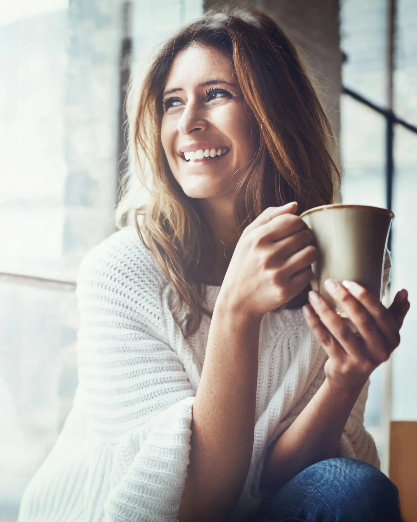 woman sitting at a window looking out while drinking a cup of tea