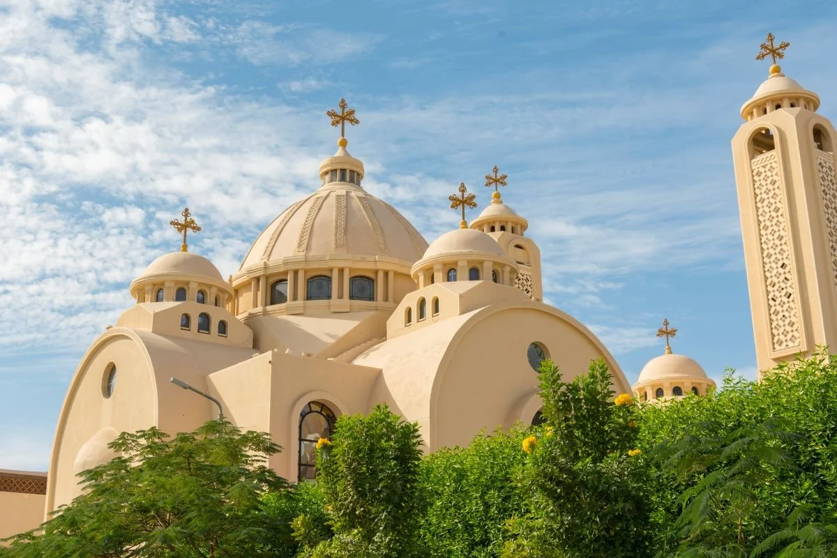 The exterior of Heavenly Cathedral show white washed walls and several domes behind a lush green tree scape