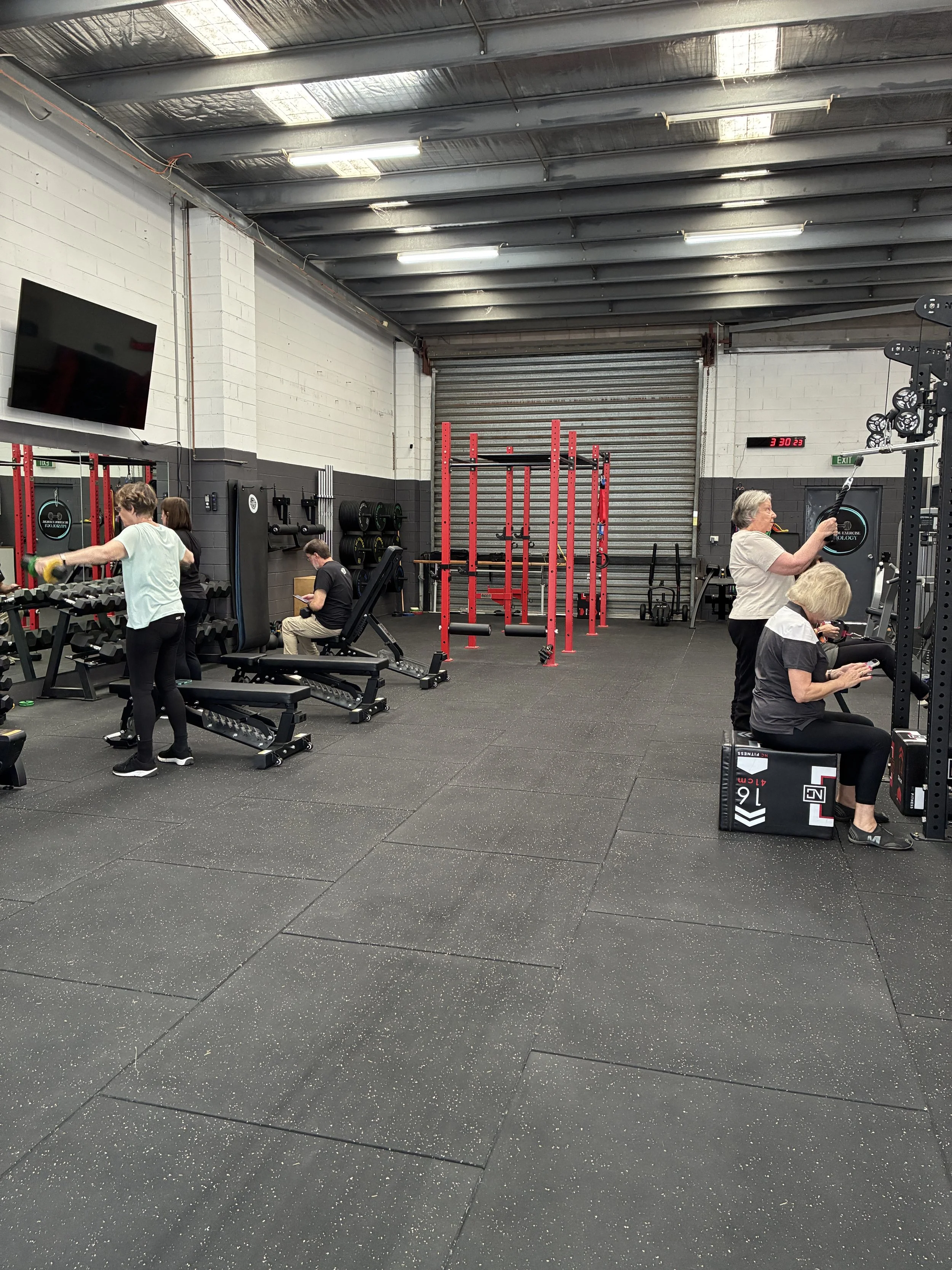 A group of people exercising in a gym with weight machines, benches, and fitness equipment.