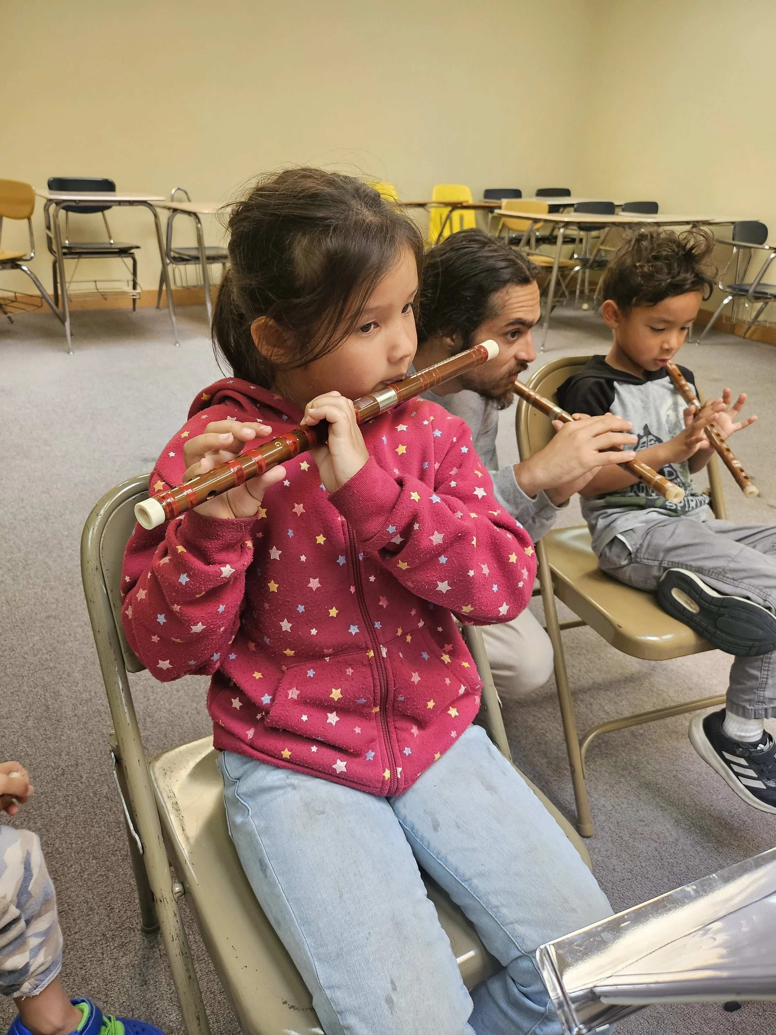 Children and an adult playing recorders in a classroom.