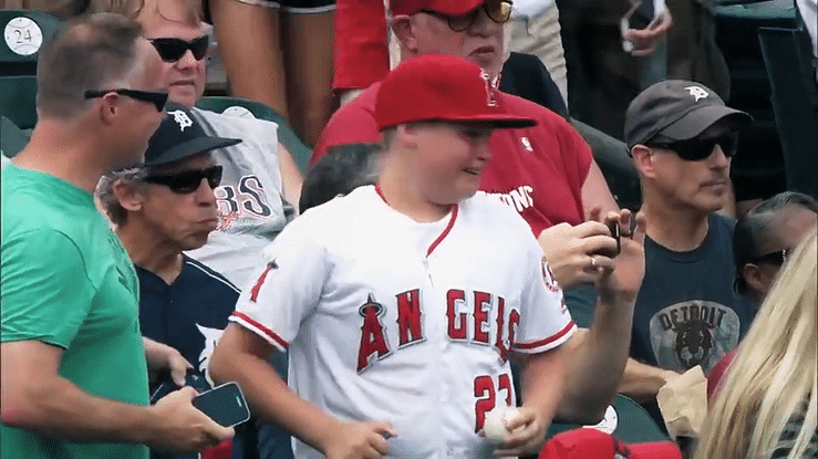 A group of baseball fans, including a young boy in an Angels jersey and red cap, at a game.