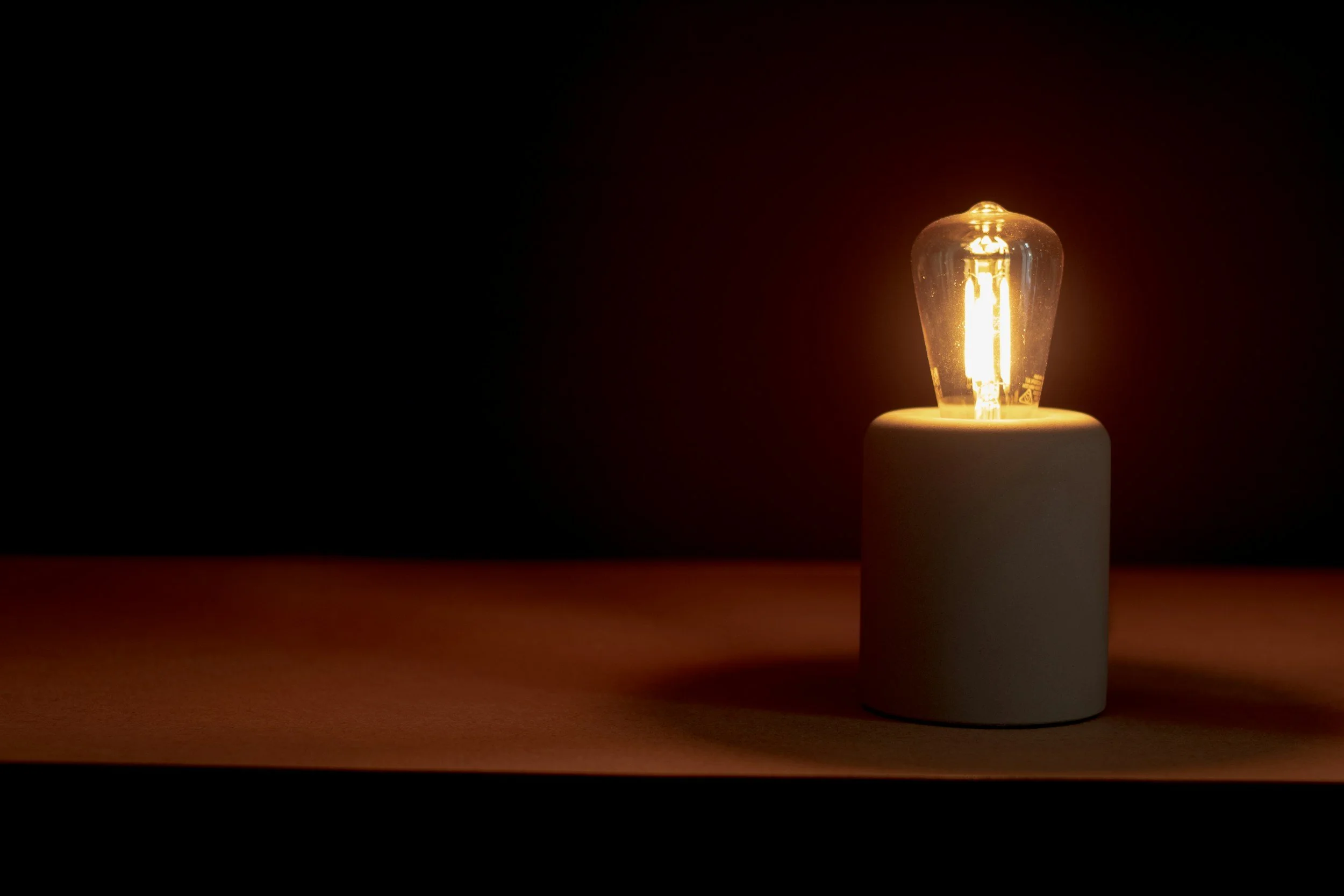 A glowing light bulb on a white cylindrical base against a dark background - representing ideas aligned to specific needs.